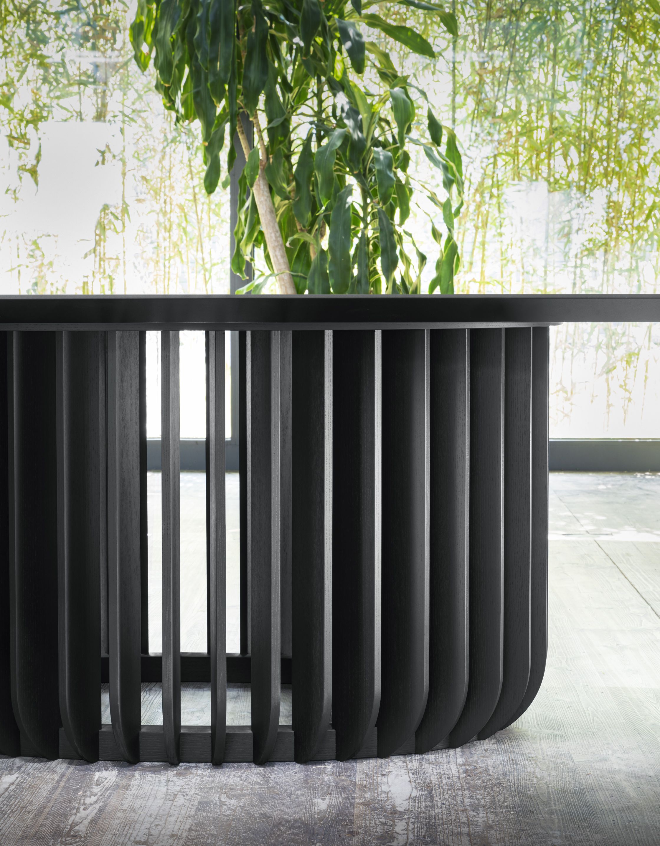 Schwarzer Juice Tisch von Miniforms mit gerippter Basis und Pflanze im Hintergrund. Designtisch für Wohnzimmer.