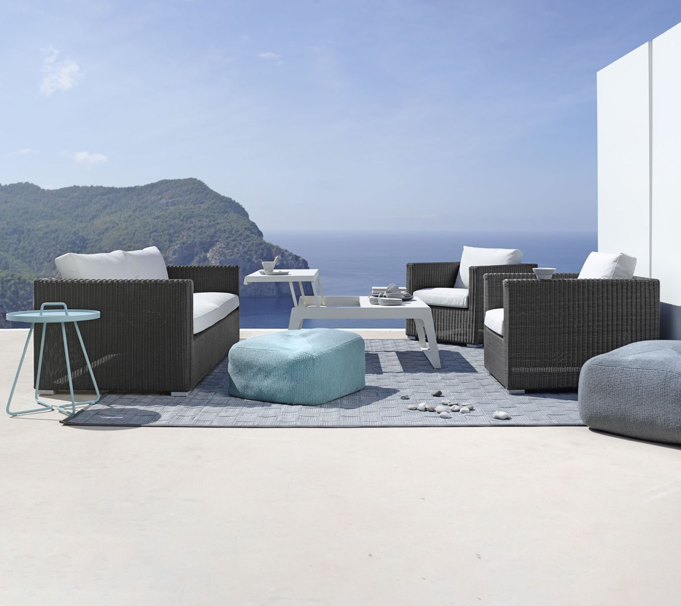 Chester Sofa: Cane-Line 3-Sitzer Outdoor-Sofa in Natur/Taupe mit weißen Kissen auf einer Terrasse.