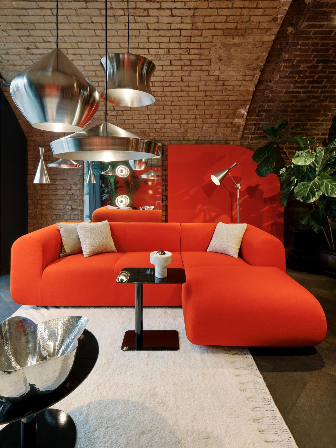 Mehrere silberne Tom Dixon Unbeaten Waist Pendelleuchten hängen über einem roten Sofa in einem Wohnzimmer.