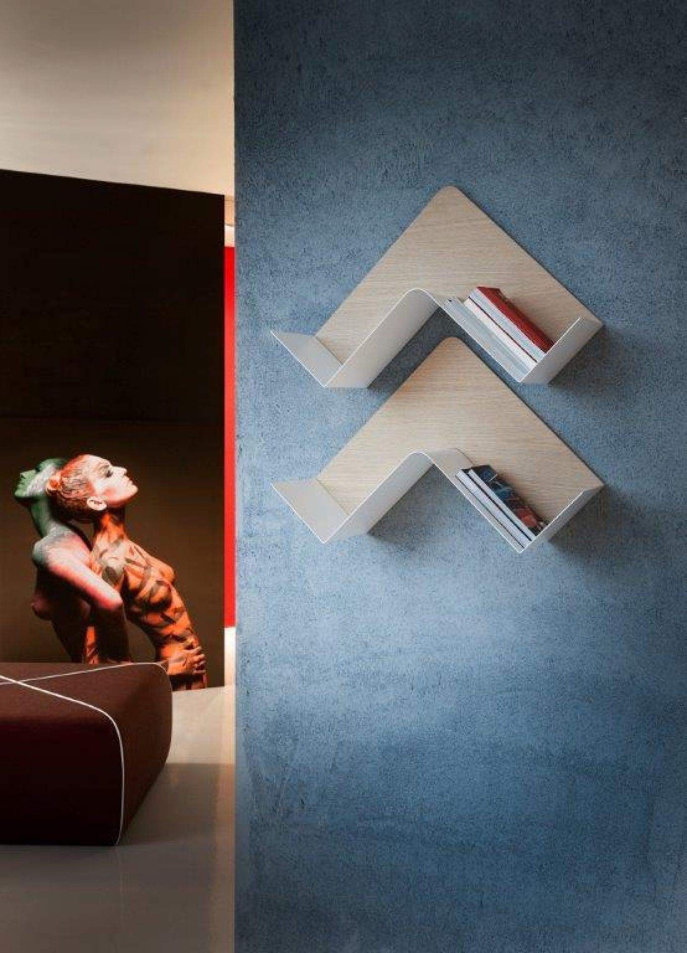 Zwei moderne, dreieckige Wandregale aus Holz und Weißmetall mit Büchern an blauer Wand.