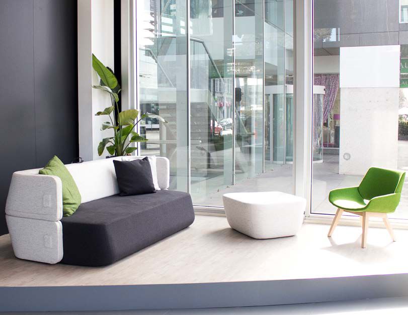 Modernes Revolve Schlafsofa von Prostoria, grauer Bezug mit Kissen, passender Hocker und grüner Stuhl.