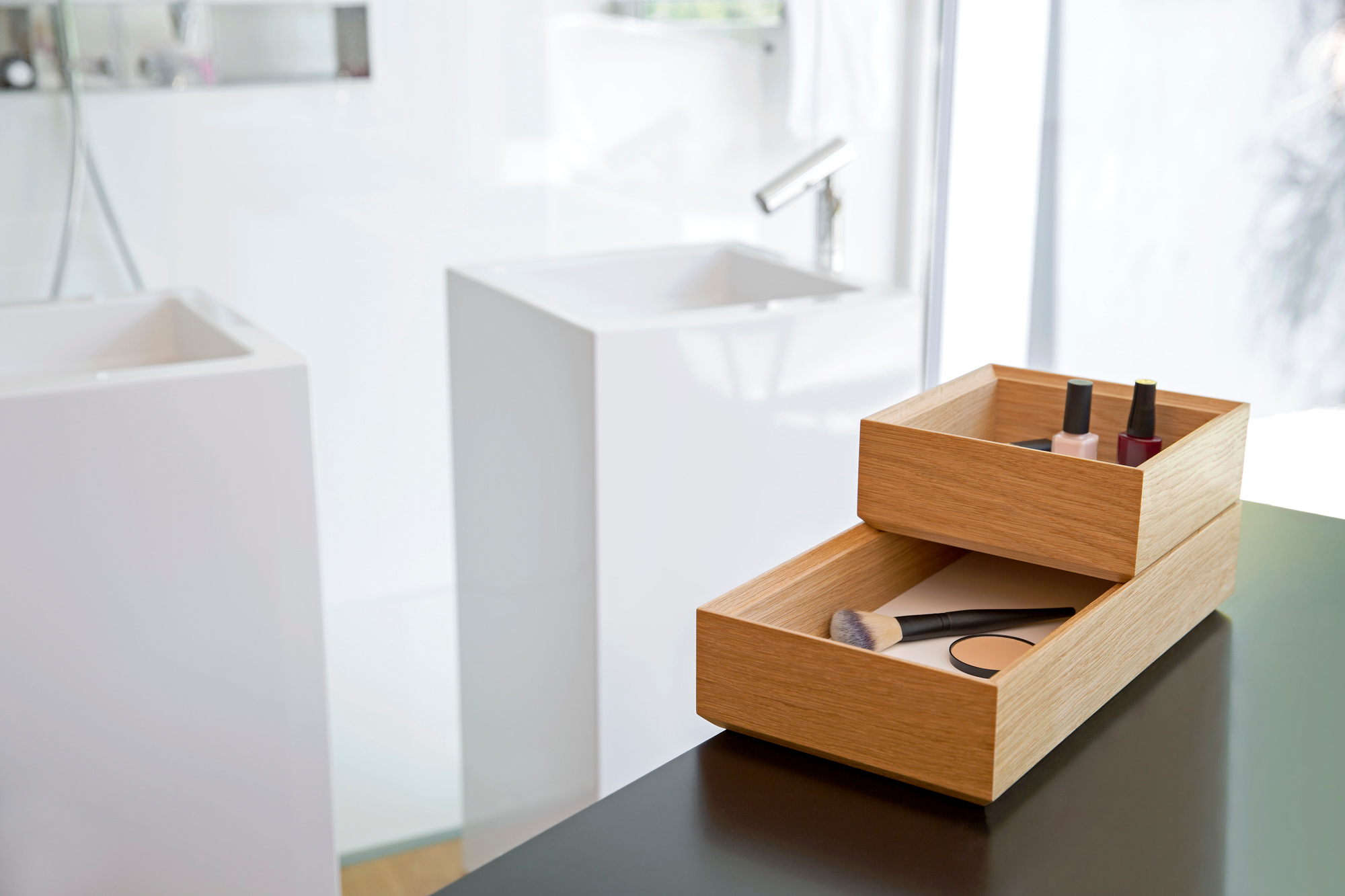 Tidy Tablett Favius 3er-Set, weiße Bad-Organizer aus Holz mit Make-up und Nagellack auf schwarzem Tisch.