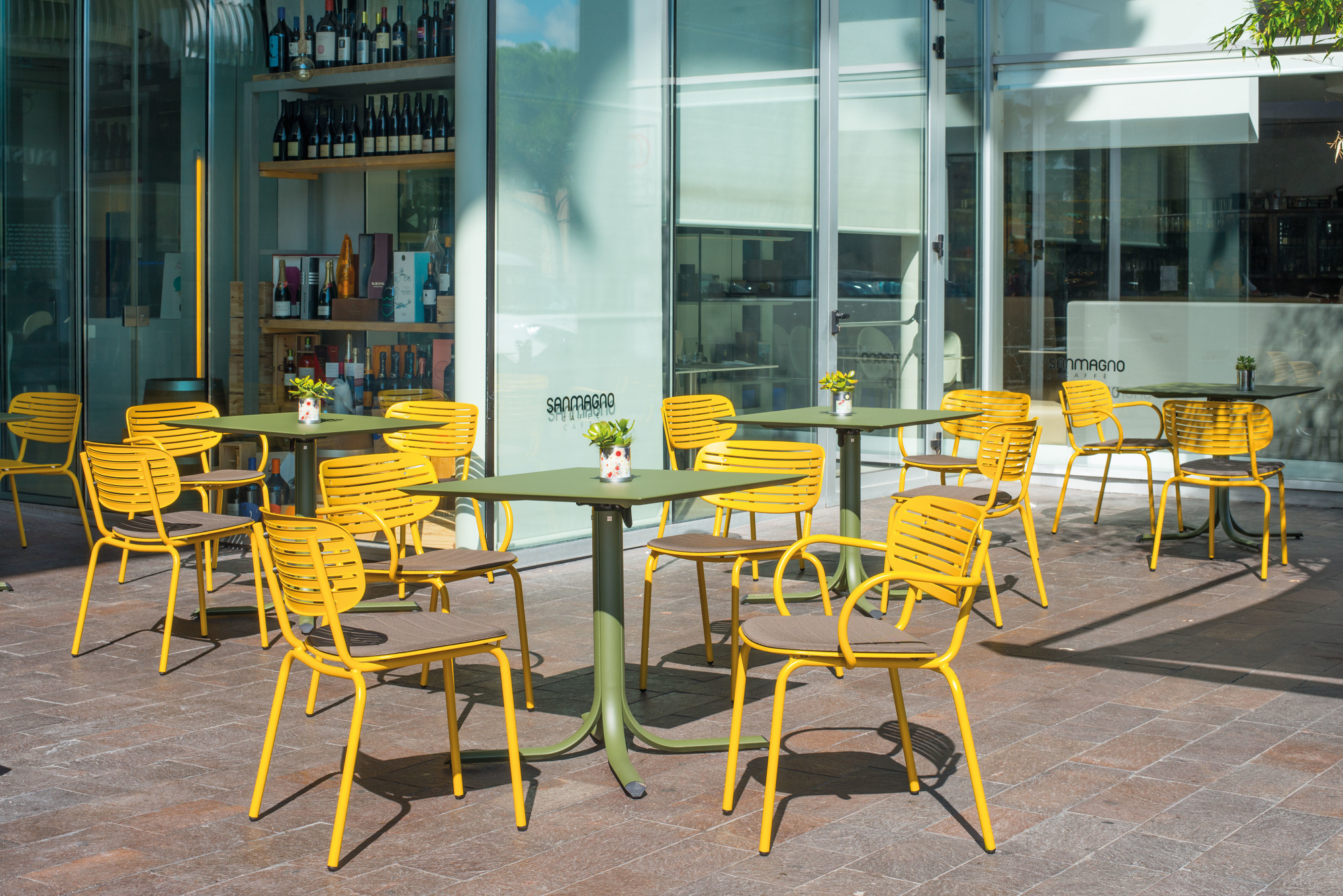 Gelbe Emu Stühle mit Armlehne und olivgrüne Tische im Außenbereich eines Cafés.