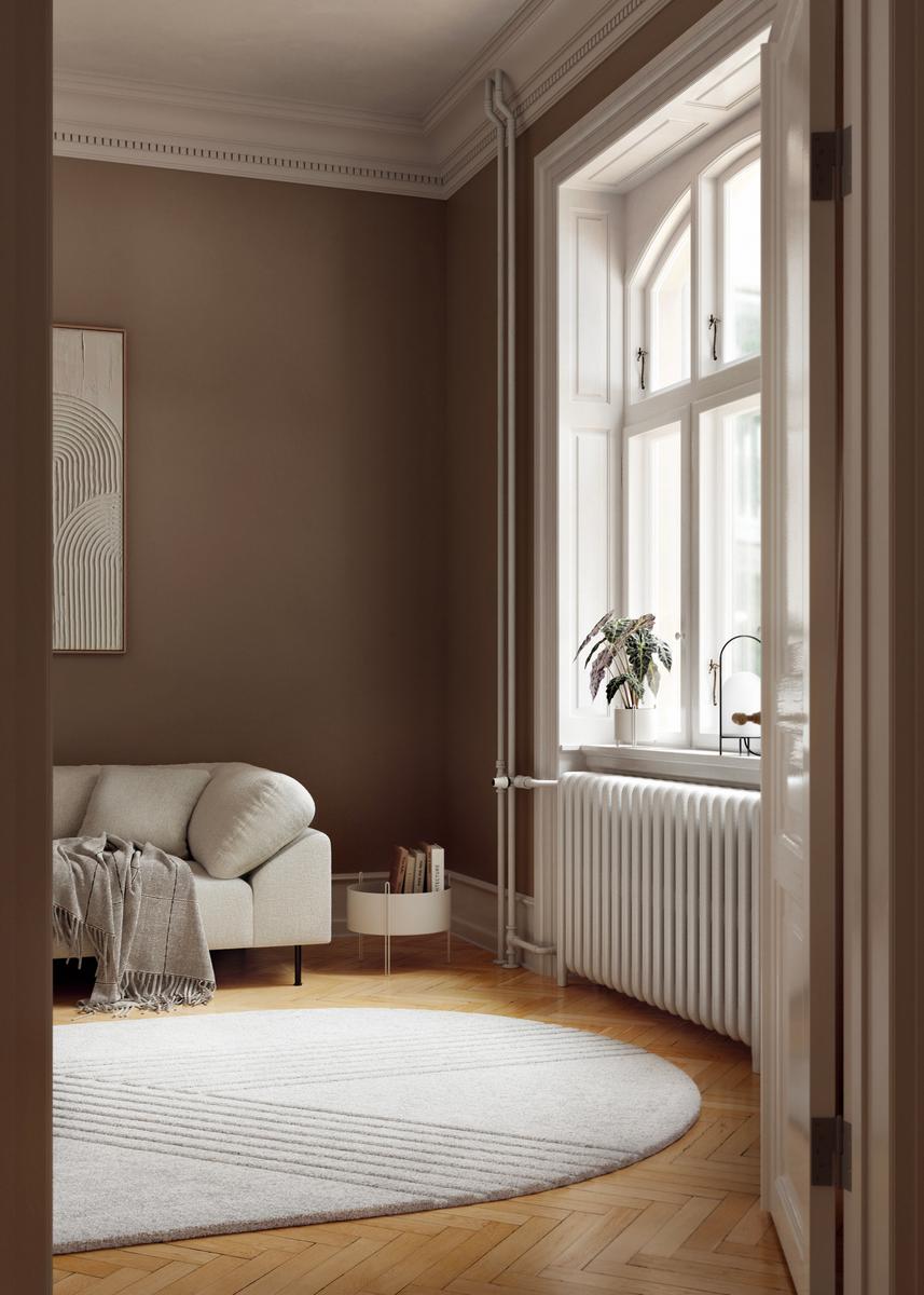 Wohnzimmer mit hellem Kyoto Teppich von Woud, Sofa und Fenster mit Heizkörper.