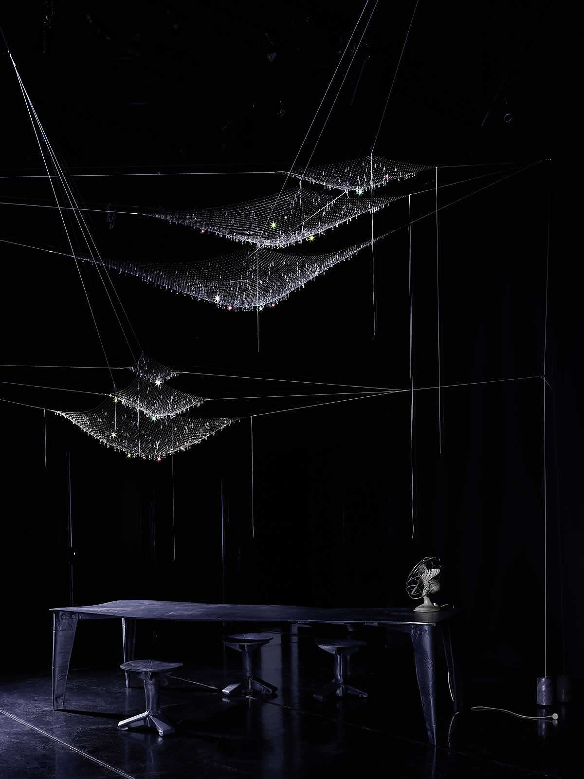 LACRIME DEL PESCATORE Pendelleuchte: Mehrere hängende, netzartige Leuchten mit glitzernden Akzenten über einem Tisch.