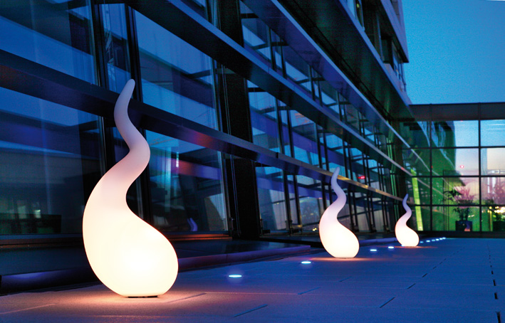 Drei Alien SL Outdoor Standleuchten M Next vor einem modernen Gebäude, stimmungsvolle Gartenbeleuchtung.