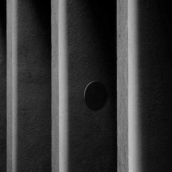 Detailaufnahme: Runde, schwarze Camouflage Wandleuchte von Flos an einer strukturierten, dunklen Wand.