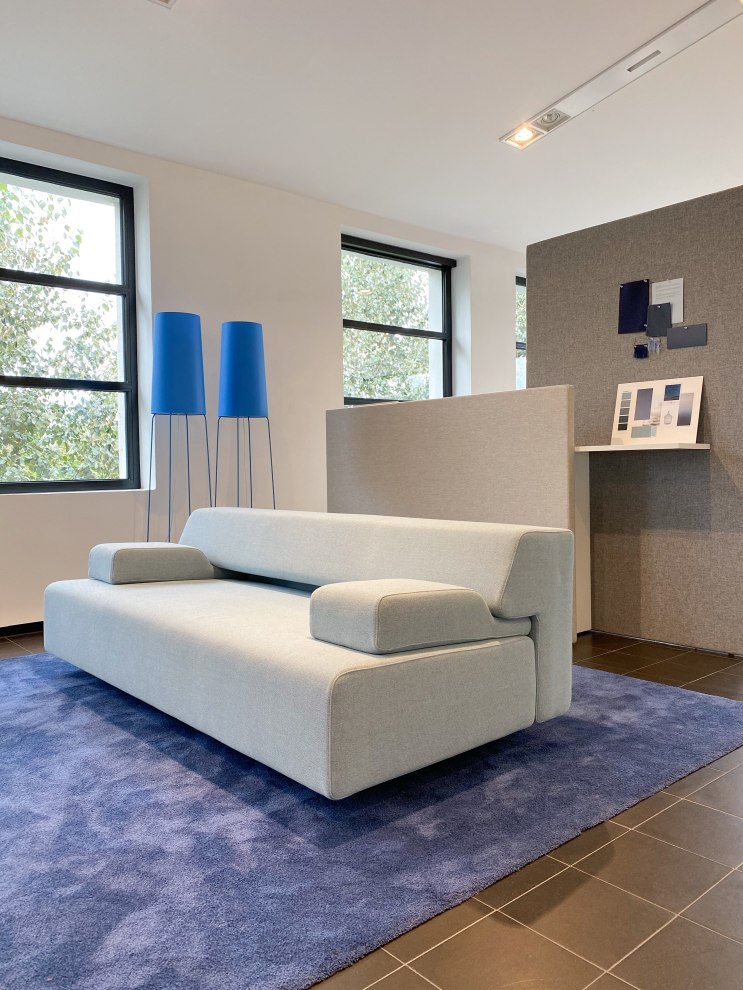 Helles Cosma Schlafsofa mit Armlehnen auf blauem Teppich, modernes Design für Wohnzimmer und Gästezimmer.