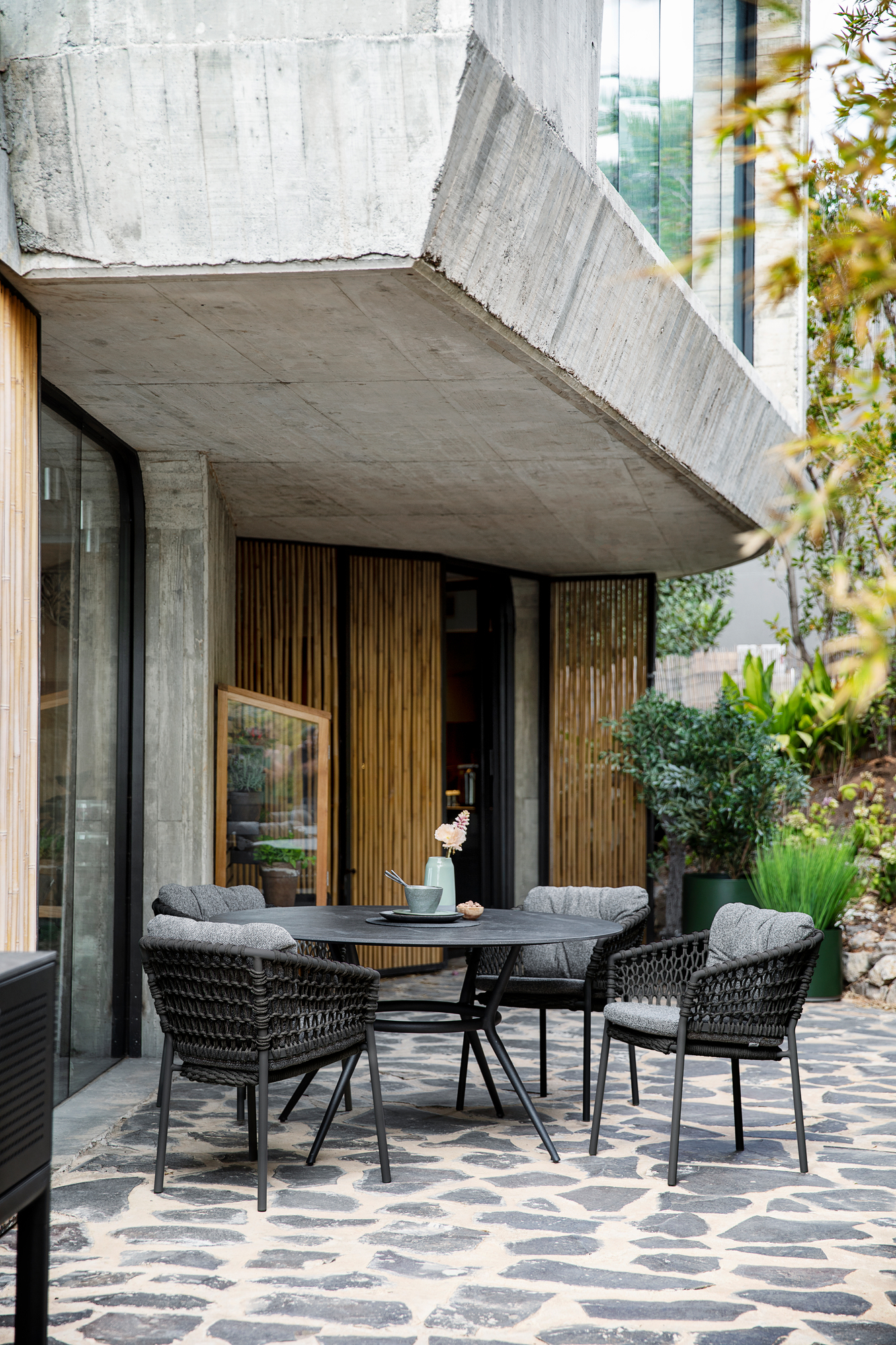 Outdoor-Szene mit Cane-Line Basket Sesseln in Umber brown mit grauen Kissen und Tisch.