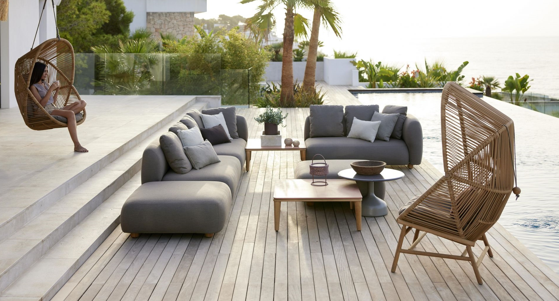 Luxuriöses Outdoor-Wohnzimmer mit grauer Lounge-Garnitur, Hängesessel und Korbsessel am Pool für entspannte Stunden.