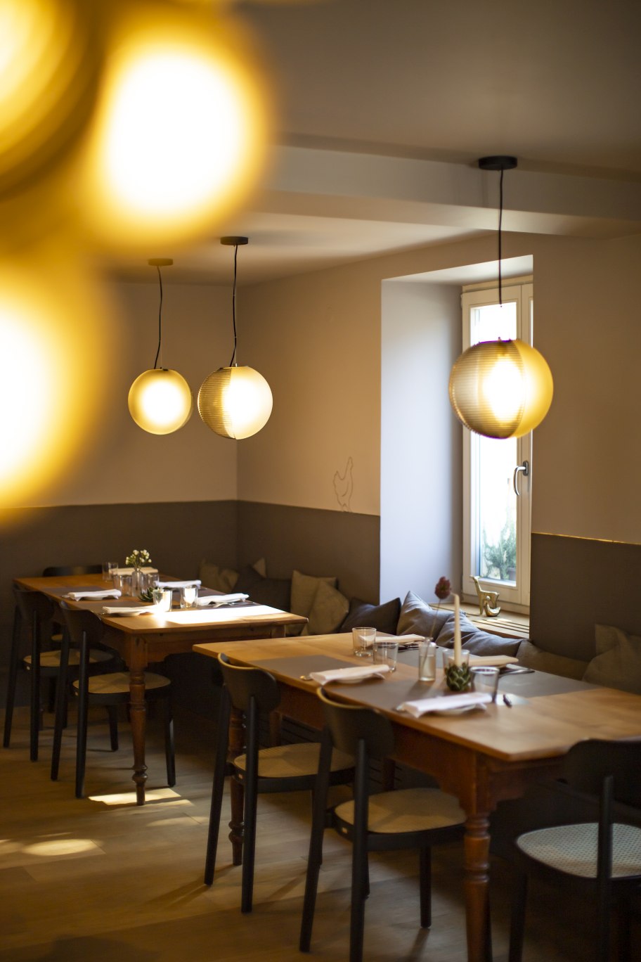 Innenaufnahme mit mehreren Stellar Pendelleuchten von Pulpo in Weiß über gedeckten Holztischen.