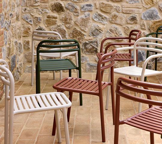 Mehrere Cane-Line Bliss Stühle in verschiedenen Farben vor einer Steinwand. Outdoor Möbel.