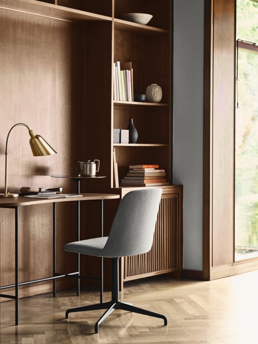 AndTradition JH9 Sekretär/Schreibtisch aus Holz mit grauem Bürostuhl und goldener Lampe vor Bücherregal.