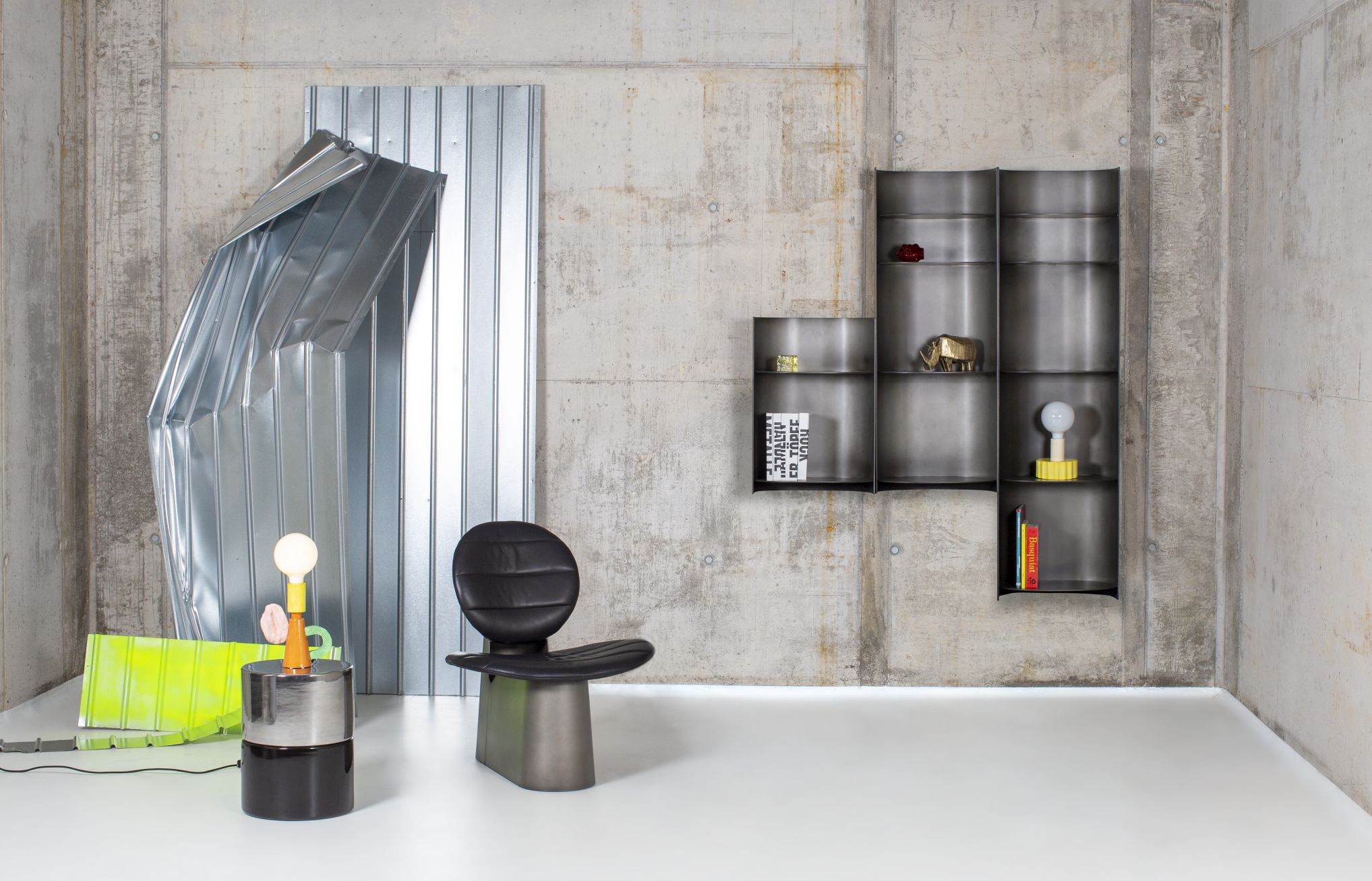 Innenaufnahme mit Como Regal, rauchgraues Metallregal, Lampe und Stuhl vor Betonwand.