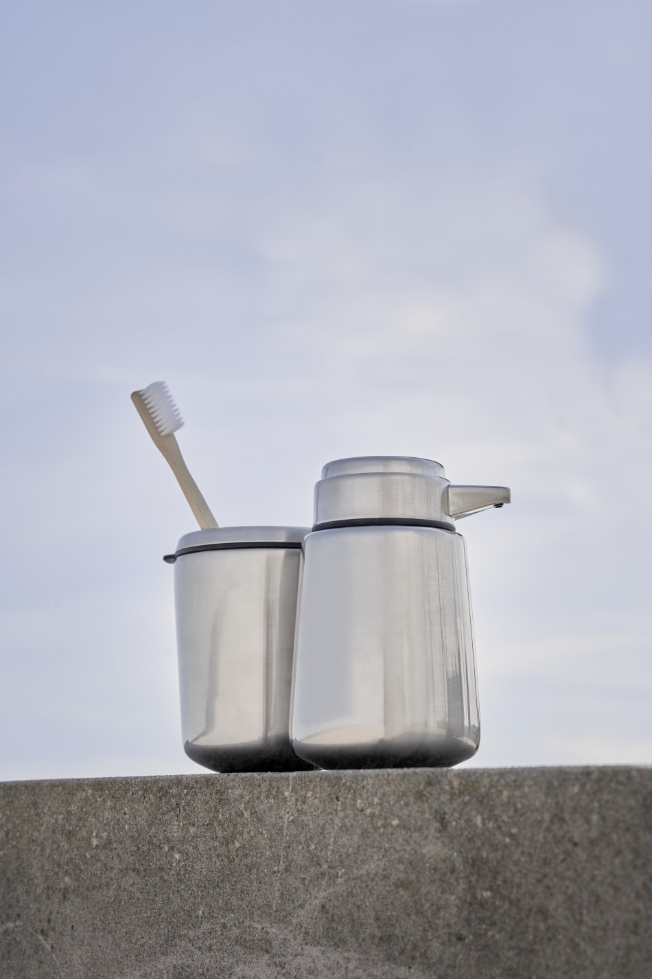 Vipp Seifenspender aus Edelstahl neben einem Becher mit Zahnbürste, modernes Badezimmer-Accessoire.