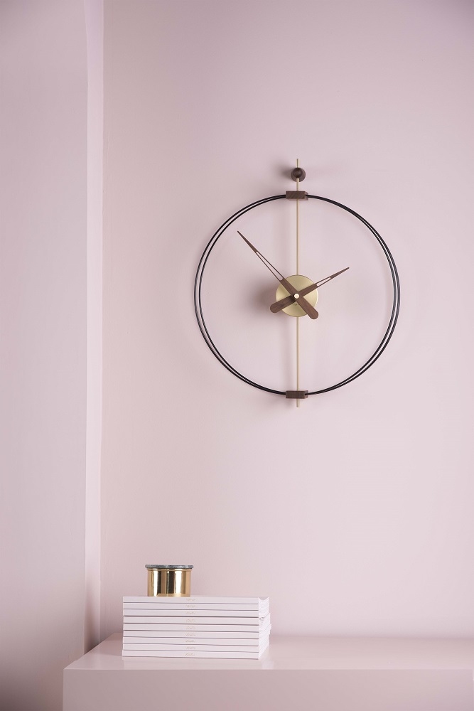 Schwarze Micro Barcelona Wanduhr von nomon an rosa Wand, minimalistisches Design mit goldenen Akzenten.