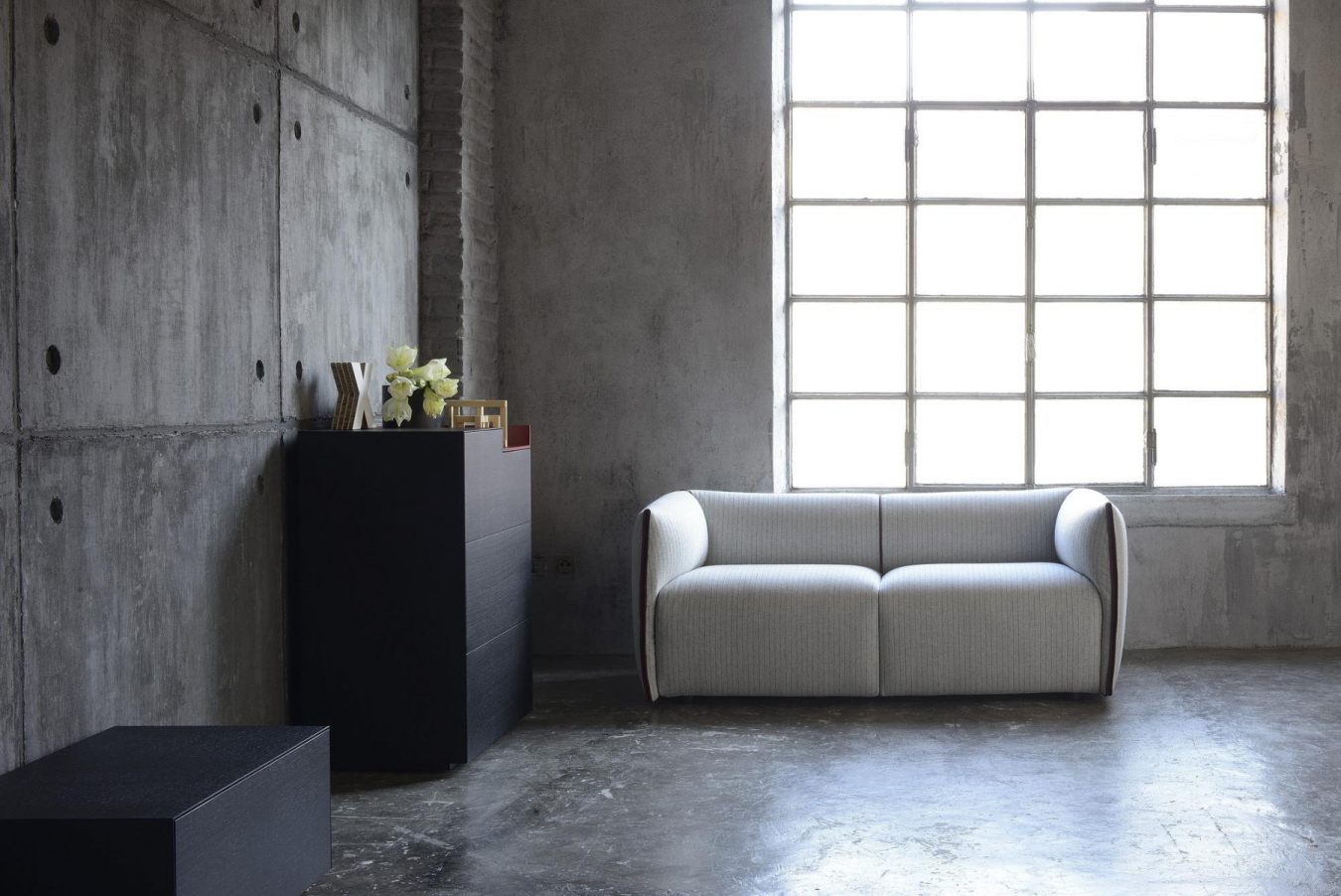 Helles, modernes 2-Sitzer Sofa in Grau vor Fenster, mit schwarzer Kommode und Dekoration.