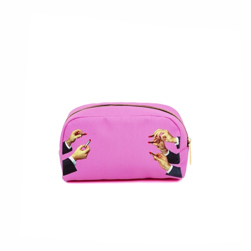 Toiletpaper Cosmetic Kosmetiktasche von Seletti mit pinkem Hintergrund und Händen mit rotem Nagellack und Lippenstift.