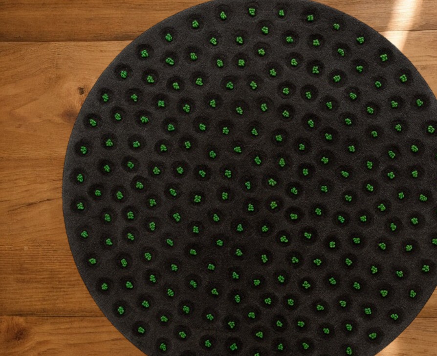 Runder La Geria Teppich von Gan, anthrazitfarben mit grünen Akzenten, auf Holzboden.