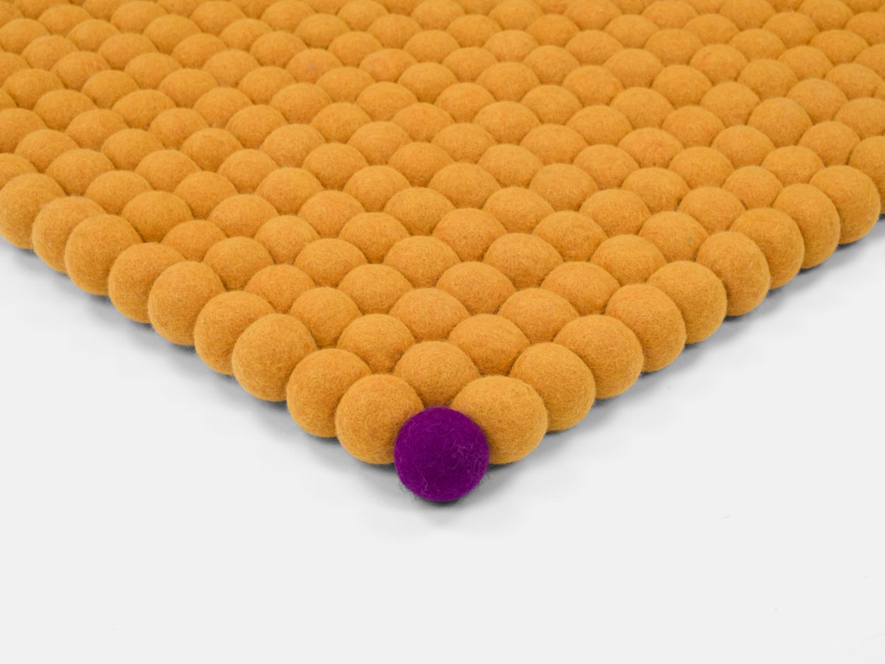 Detailaufnahme: Gelber Filzteppich "Big One" von myfelt (140x200cm) mit einer einzelnen lila Filzkugel.