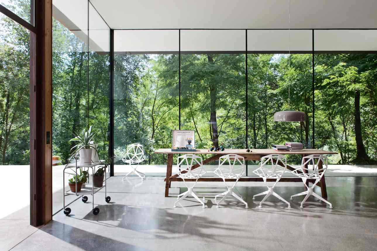 Helle Inneneinrichtung mit Magis Chair One Stühlen und Viersternfuss an einem Holztisch vor Fensterfront.