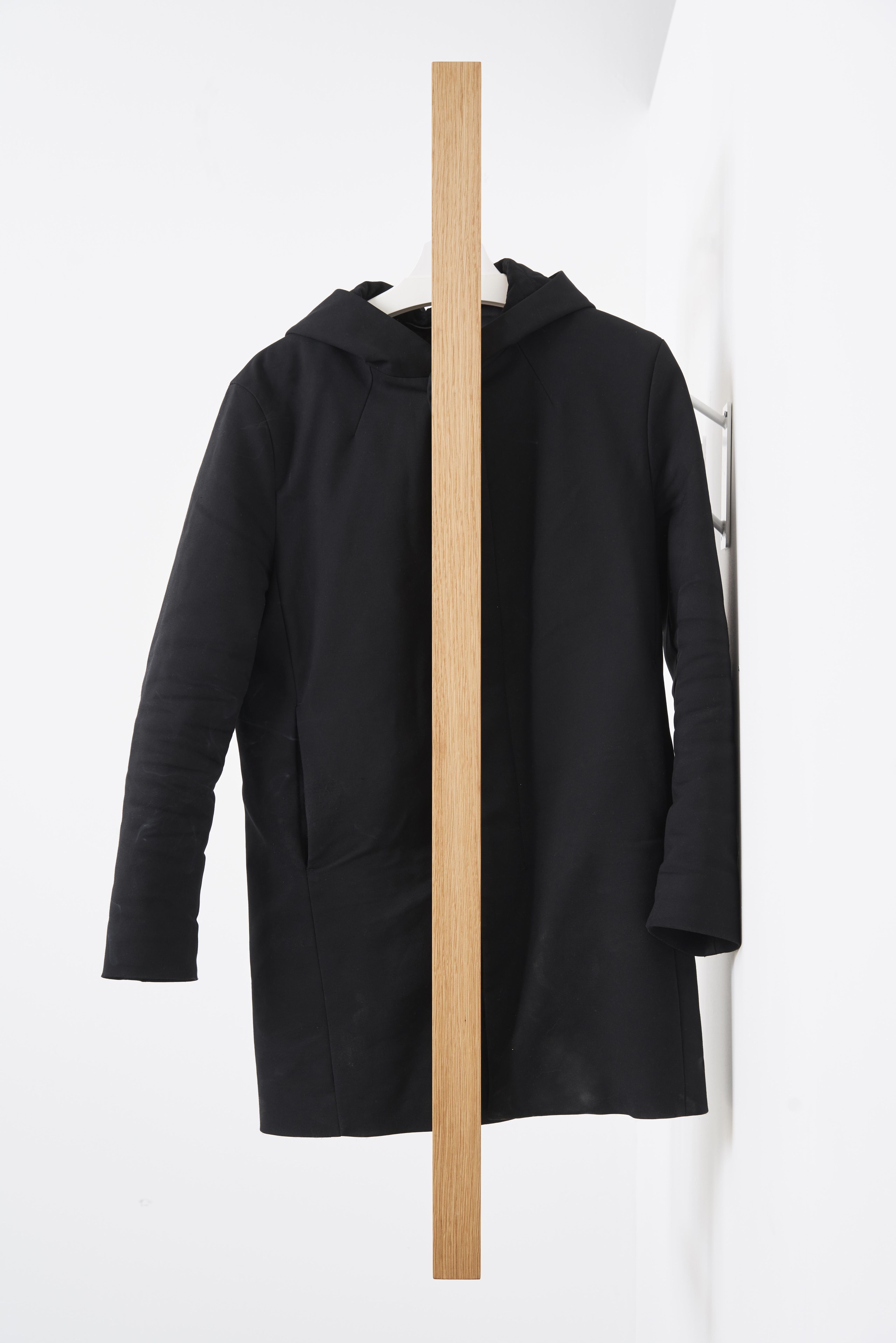 Schwarzer Mantel hängt an der gardero-b Wandgarderobe aus hellem Holz. Moderne Garderobenlösung für Flur und Eingangsbereich.