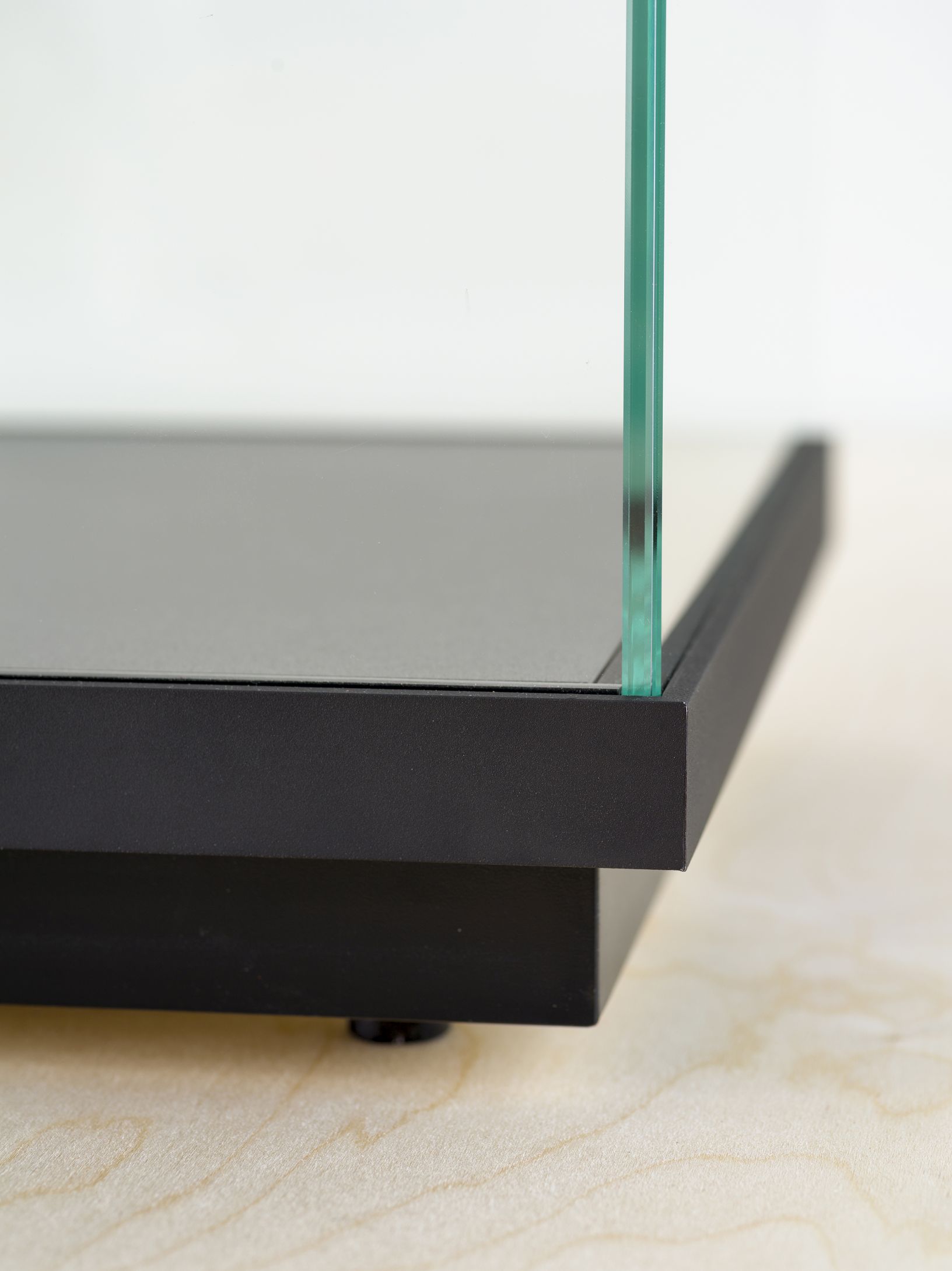 Detailaufnahme der Stolp Low Vitrine: Schwarzer Sockel mit Glaswand auf hellem Holzuntergrund. Funktionale Möbel für Wohnraum.