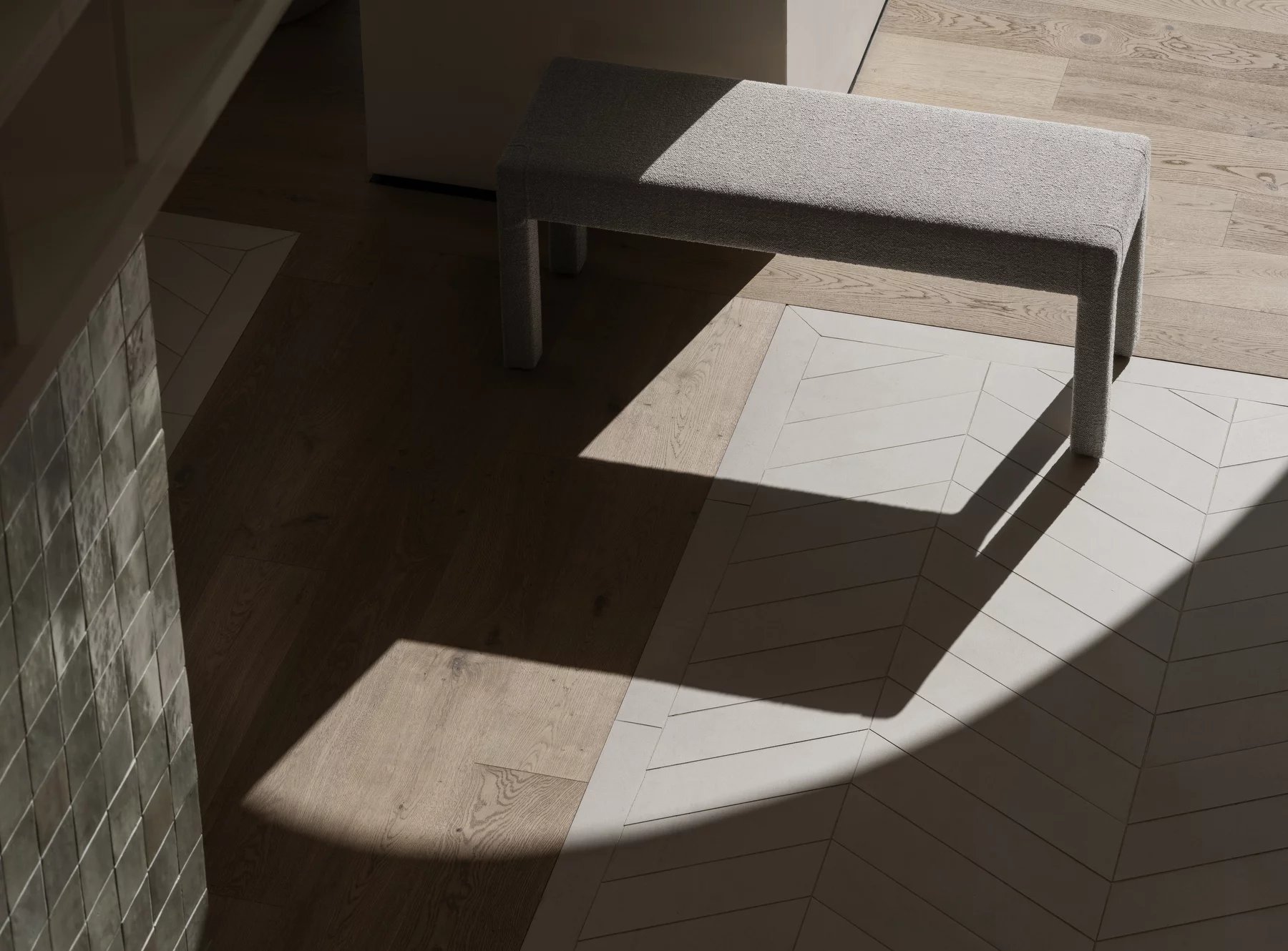 Nahaufnahme der grauen Blomus Sitta Bank auf hellem Holzboden mit Schatten. Moderne Sitzbank für zwei Personen.