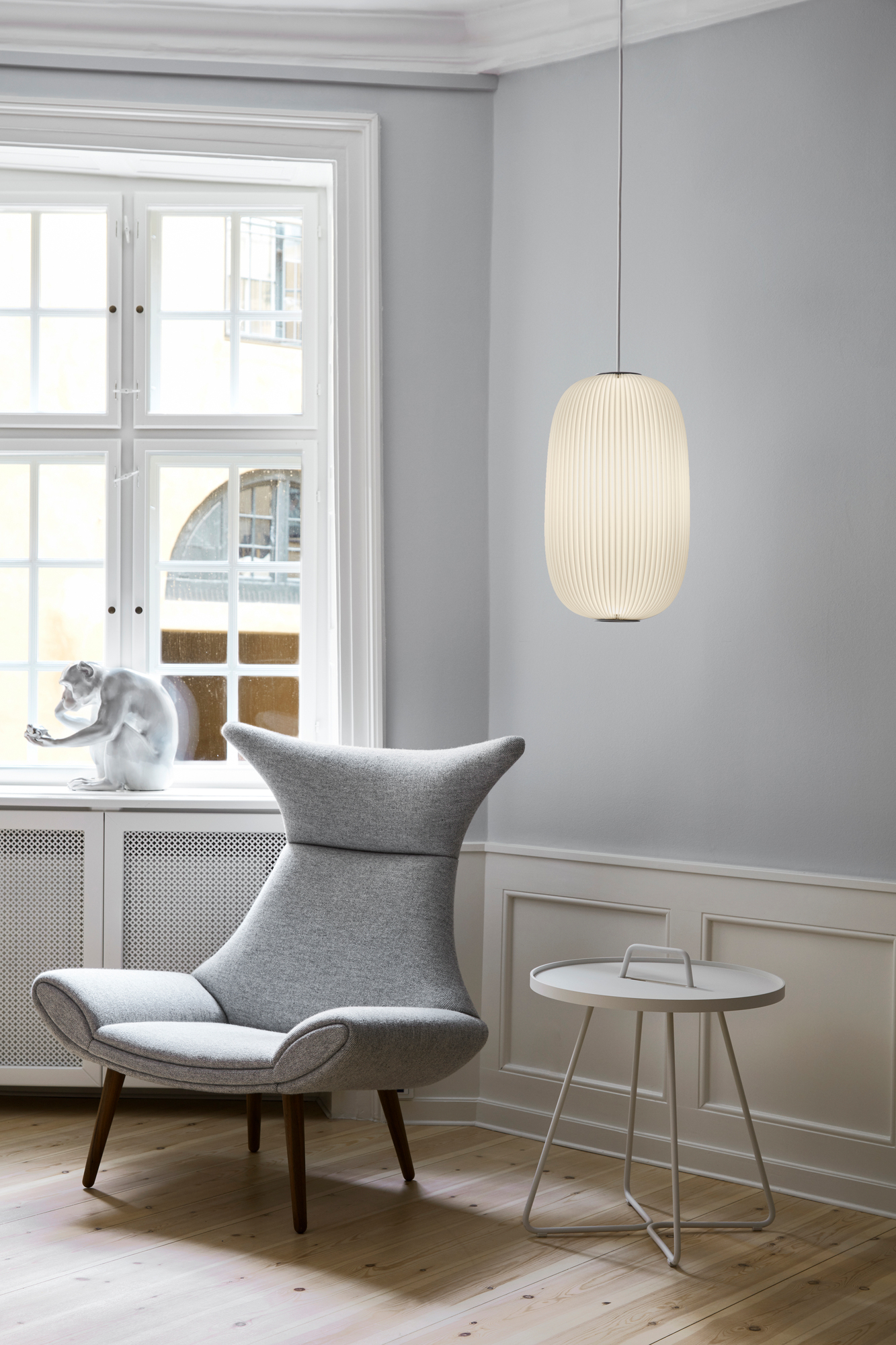 Helle Lamella Pendelleuchte von Le Klint im modernen Wohnzimmer mit Sessel und Beistelltisch.