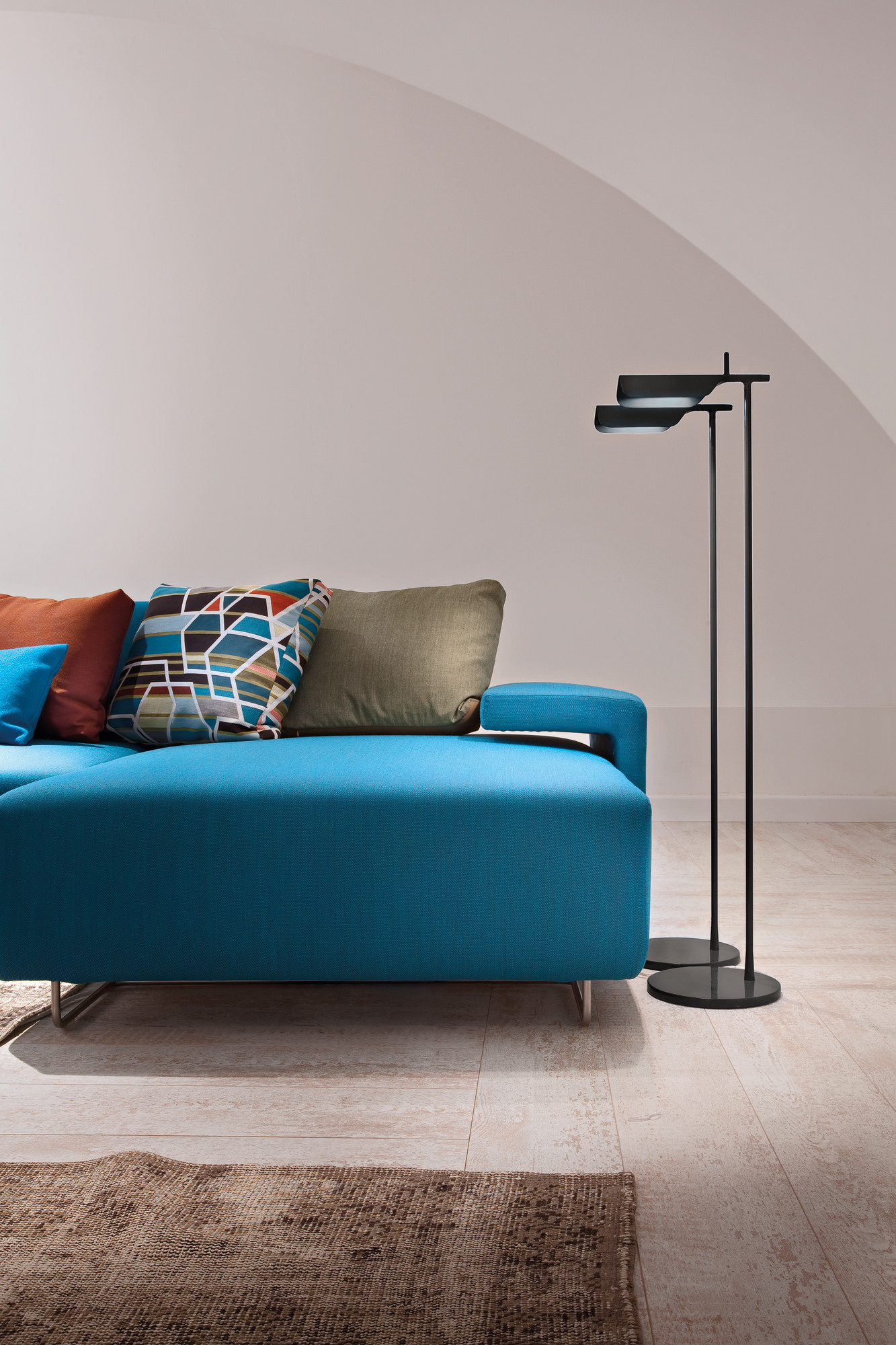 Tab F LED Stehleuchte von Flos neben einem blauen Sofa im modernen Wohnzimmer.