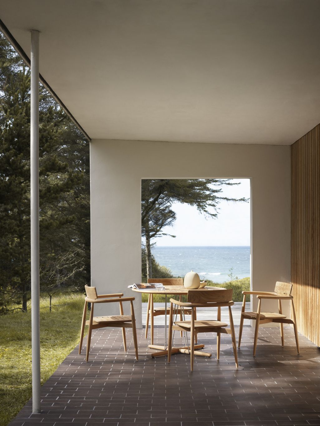E008 Embrace Stuhl von Carl Hansen & Søn aus Holz auf einer Terrasse mit Meerblick.