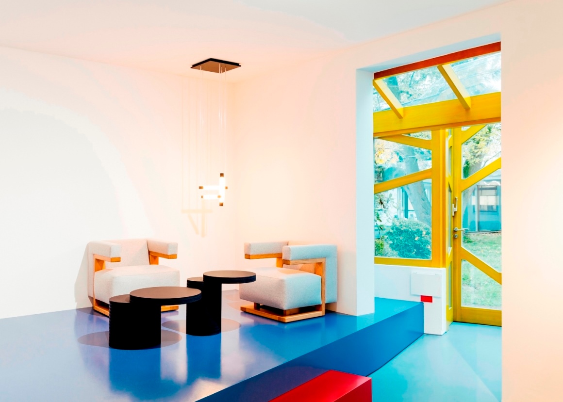 Minimalistisches Wohnzimmer mit Tecta K8B Couchtisch, schwarzen Beistelltischen und modernen Sesseln auf blauem Boden.