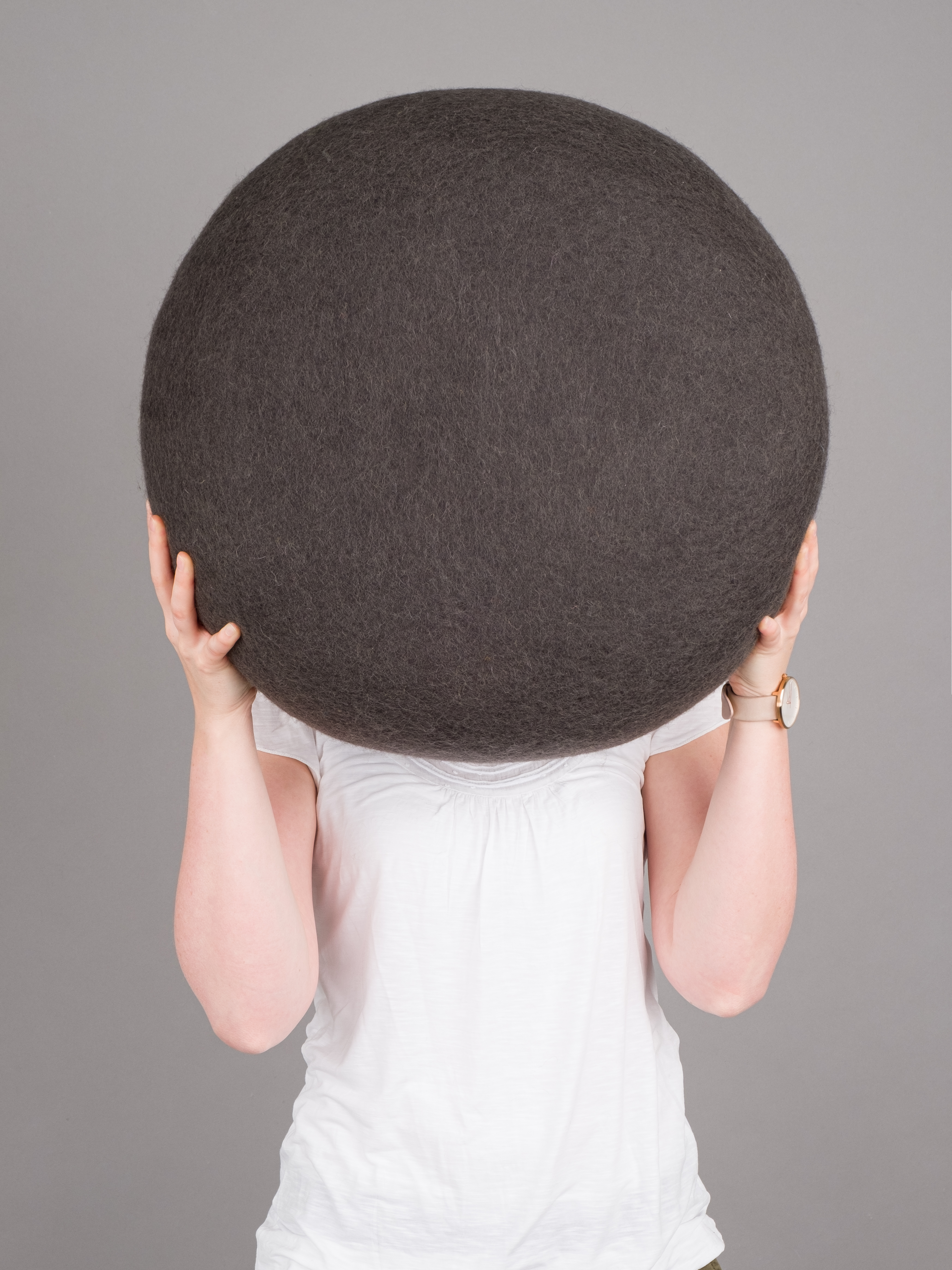 Frau hält grauen myfelt Filz Pouf Hocker M Kuno vor dem Gesicht.