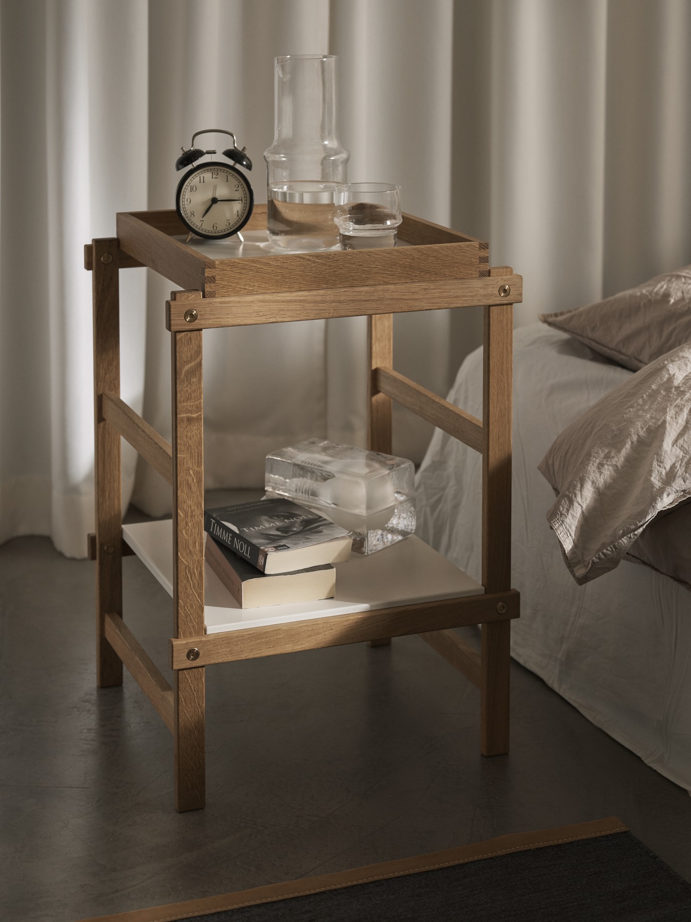 Frame Small Regal von Design House Stockholm aus Eiche mit Deko-Objekten neben einem Bett.