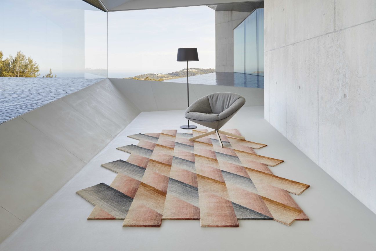 Mirage Teppich nude von Gan, abstrakter Designteppich in Rosa- und Grautönen, modernes Wohnambiente mit Sessel.