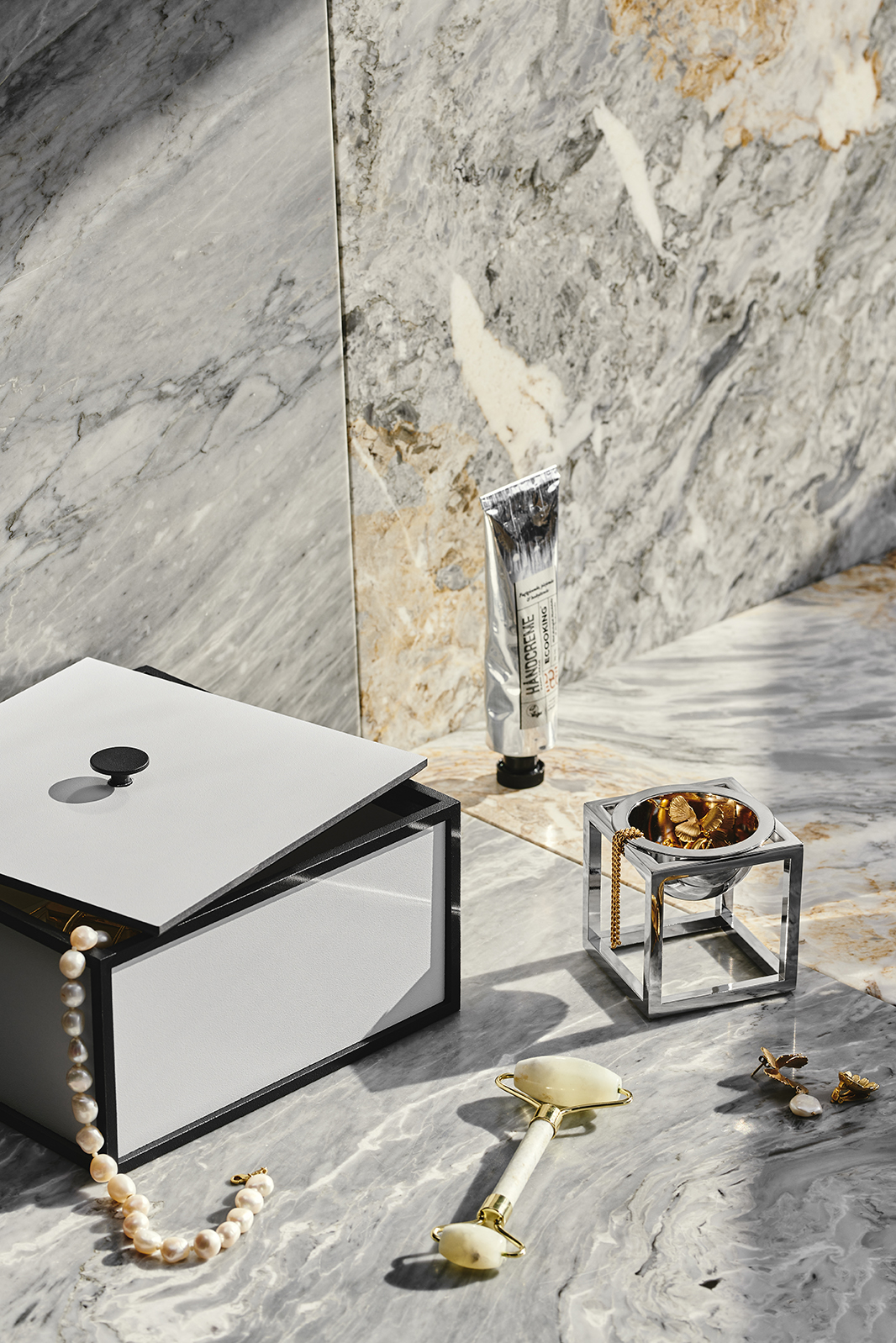 Produktfoto: Schmuckkästchen, Handcreme, Jade-Roller, Schmuck und dekorativer Behälter auf Marmor.