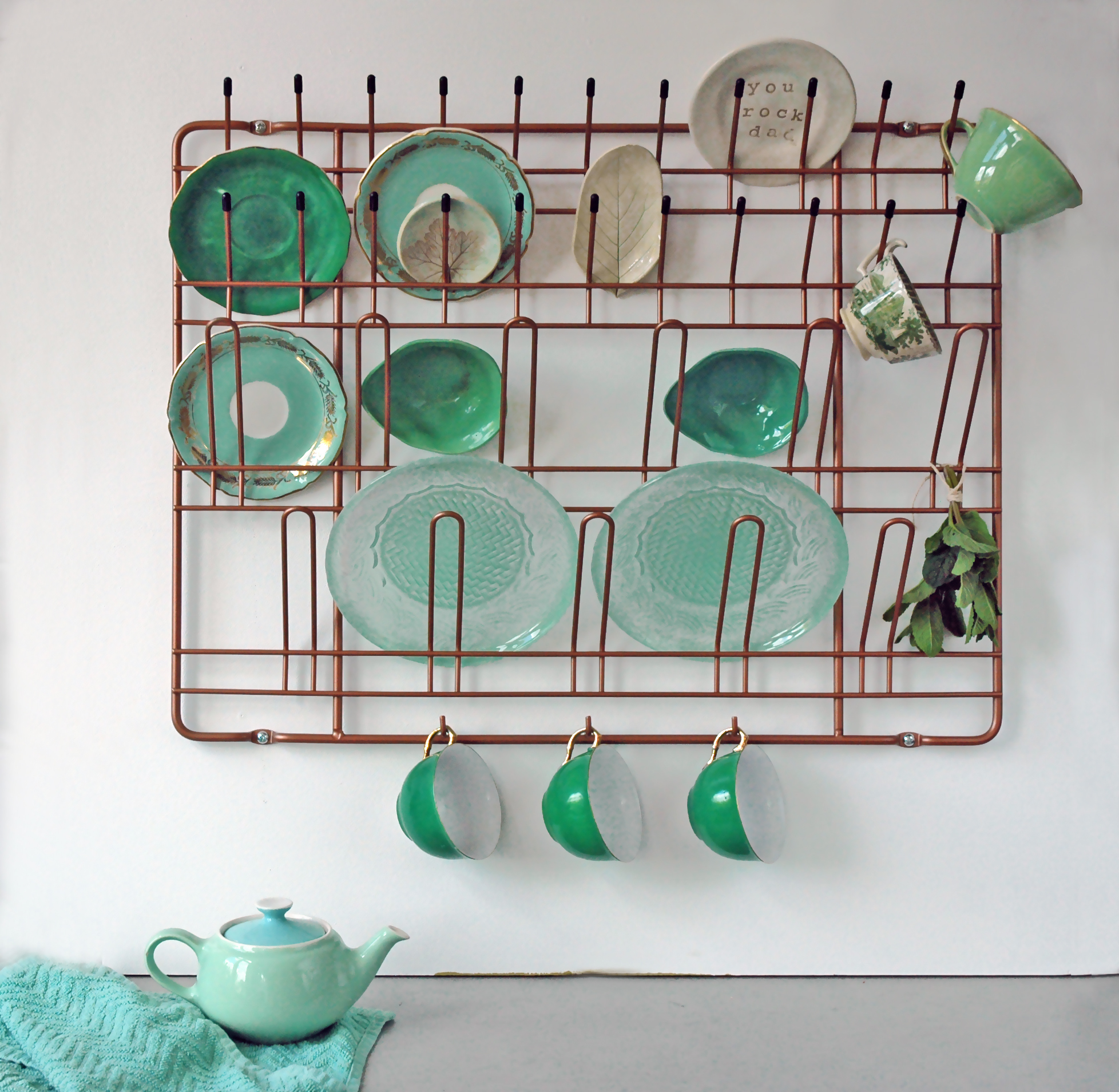 Puhlmann Stow & Hang Frame Garderobe: Kupferfarbenes Wandregal mit Geschirr und Tassen in Grüntönen.