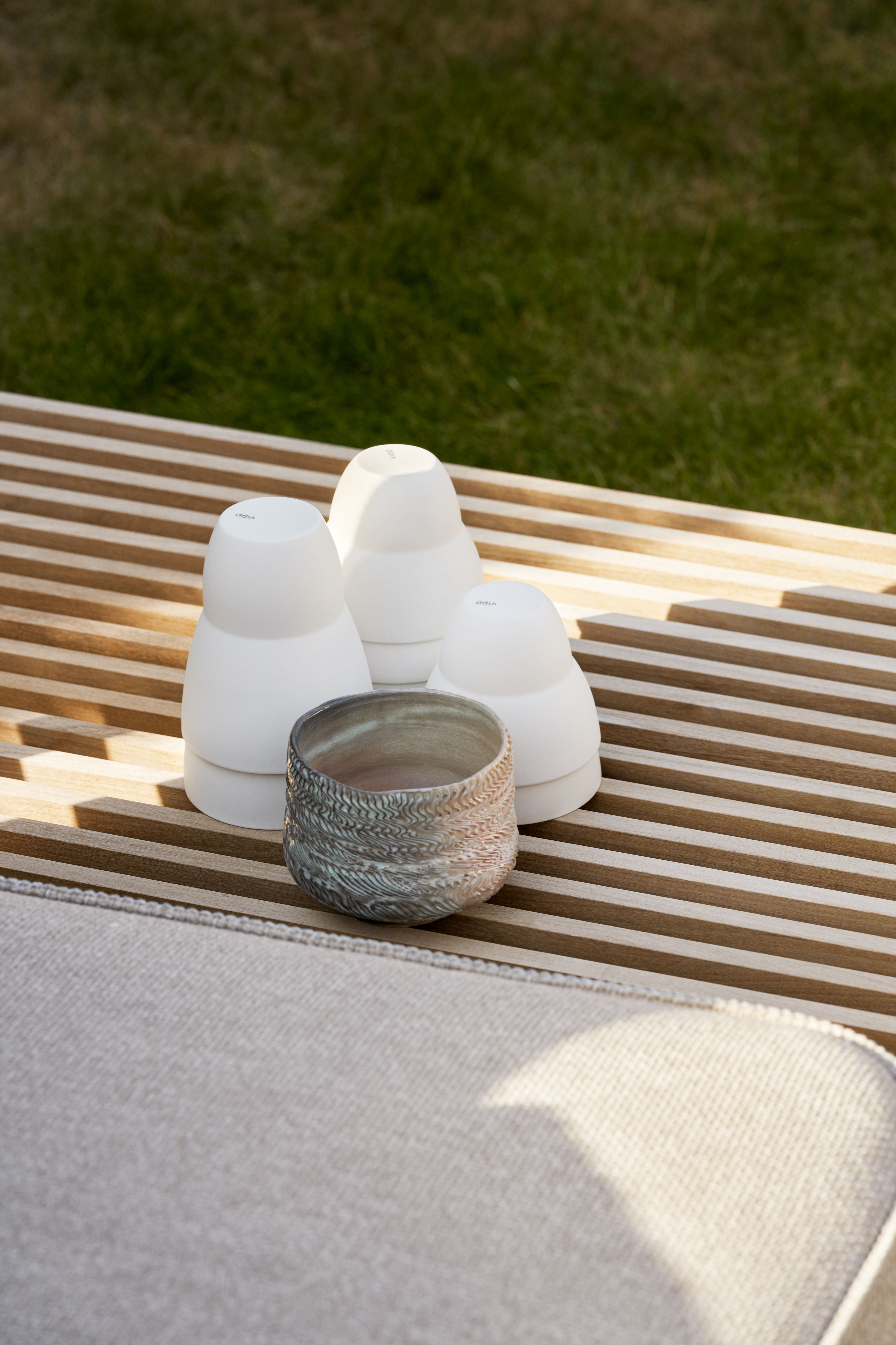 Detailaufnahme von Vipp Open-Air Outdoor Sofa mit Dekoration: Keramikvase und weißen Design-Objekten auf Holzlatten.