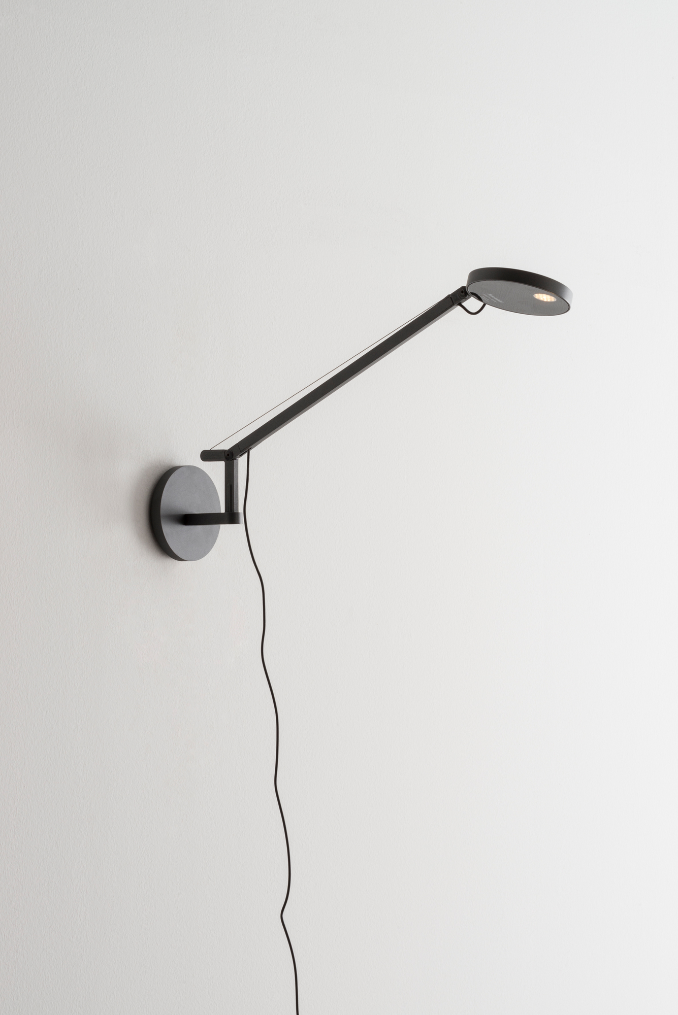 Schwarze Demetra Micro Wandleuchte von Artemide mit verstellbarem Arm und warmweißem Licht.