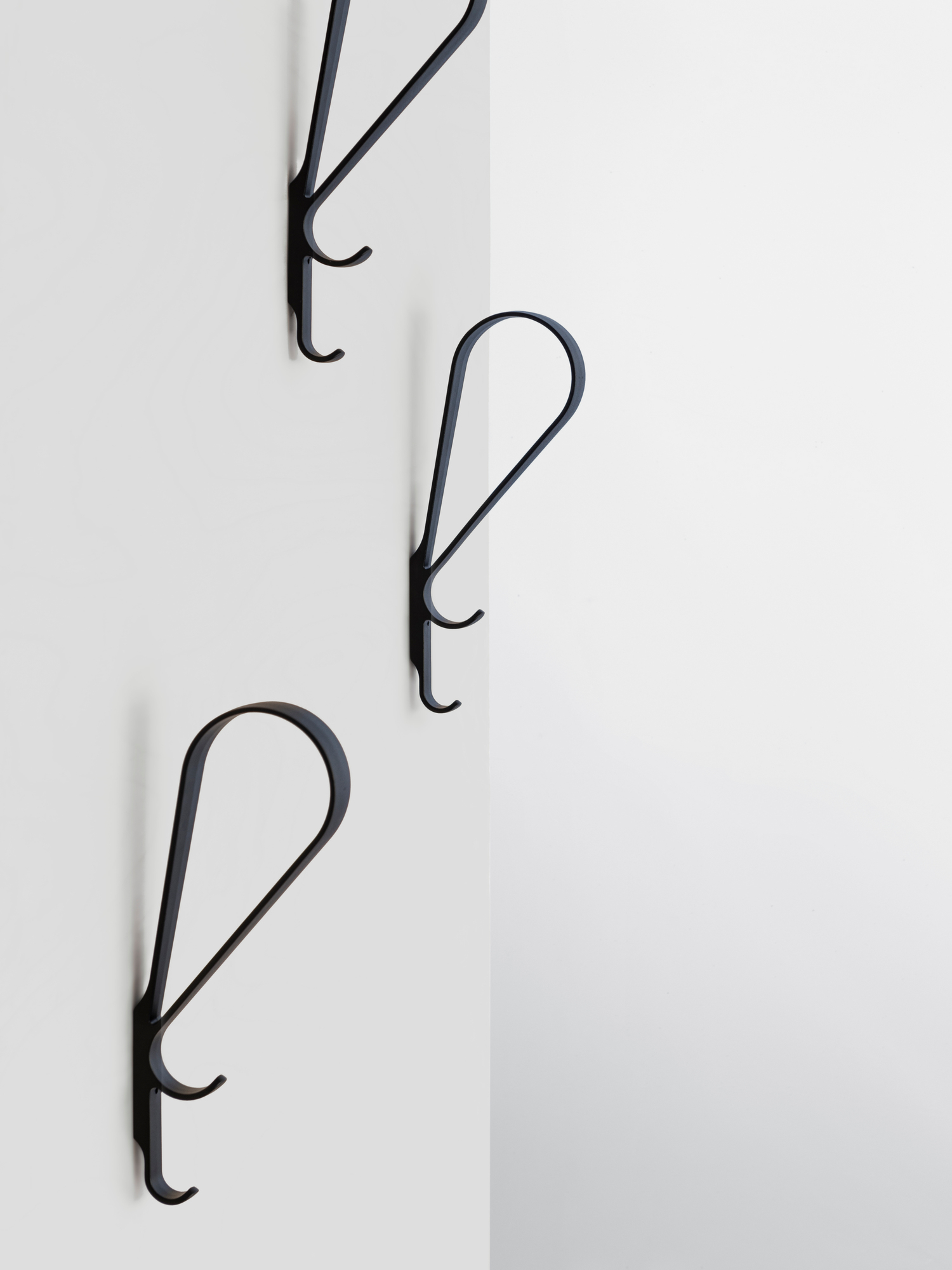 Drei schwarze Artek Tupla Wandhaken an einer weißen Wand, modernes skandinavisches Design für Garderobe und Aufbewahrung.