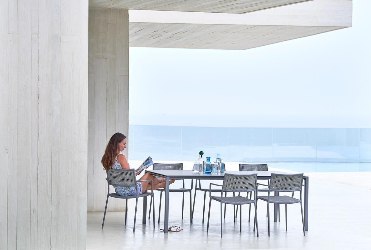 Frau liest auf Cane-Line Less Outdoor Stuhl. Stapelbarer Gartenstuhl aus wetterfestem Material.