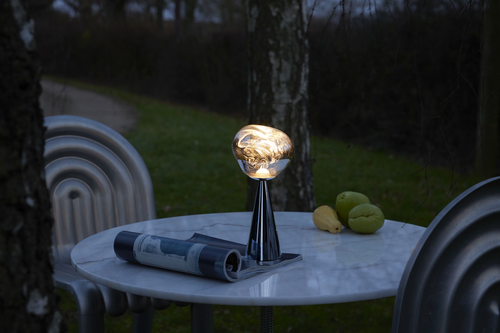 Silberne Melt LED Tischleuchte von Tom Dixon auf Marmortisch im Garten.