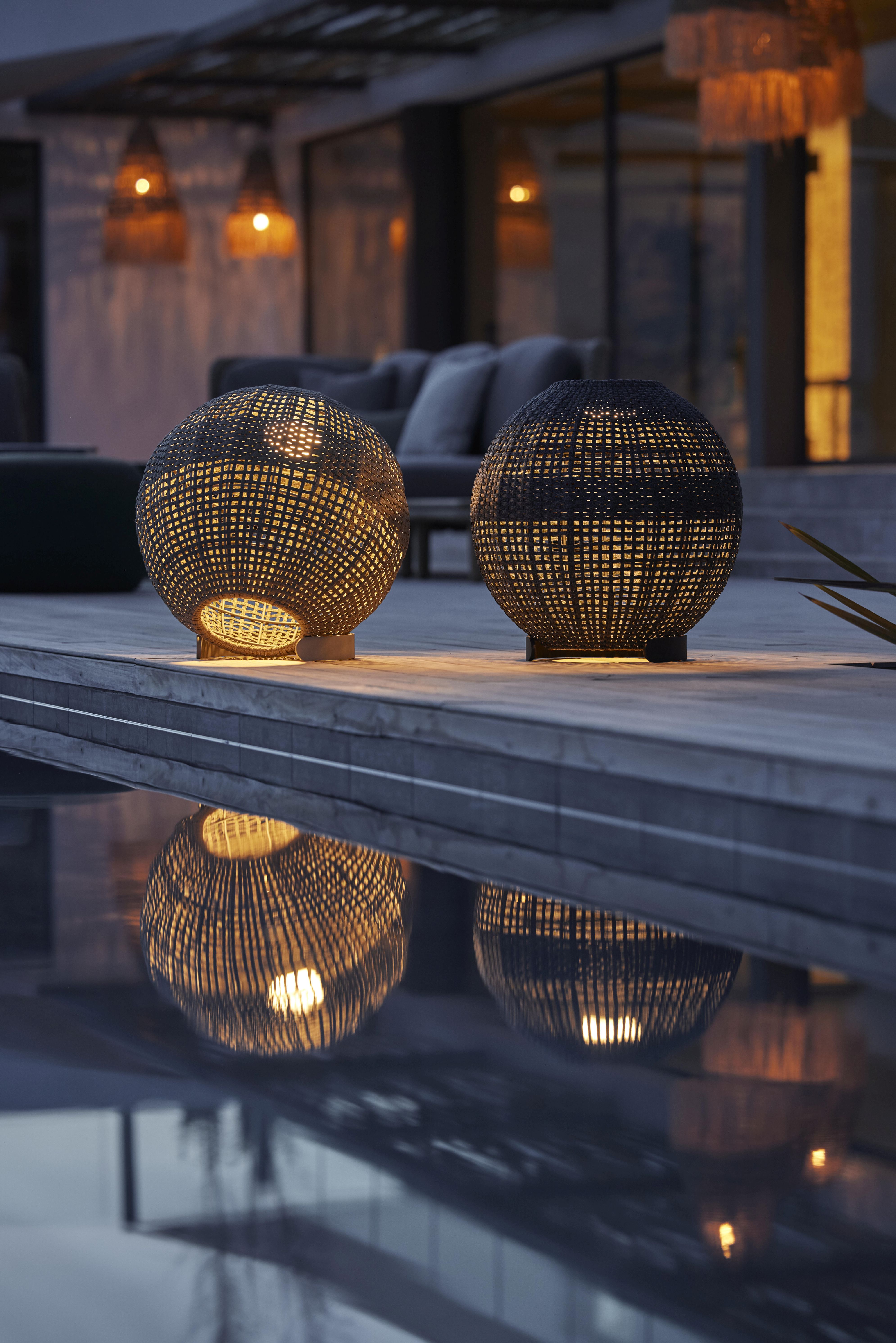 Zwei runde, dunkelgraue Cane-Line Outdoor Lampen mit Flechtmuster und warmem Lichtschein.