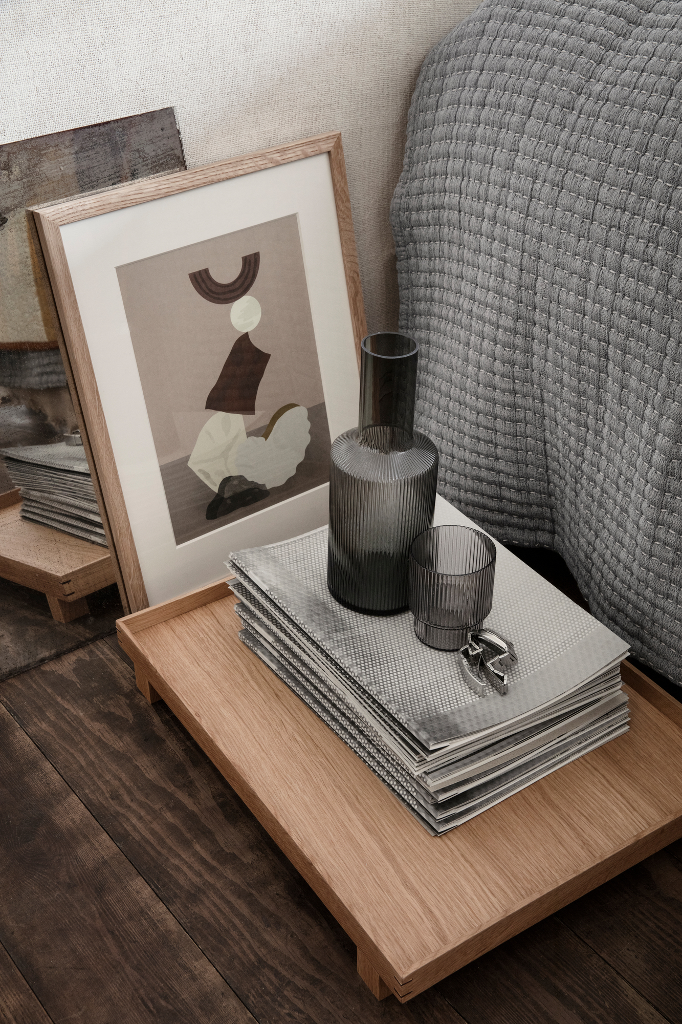 Rauchgraue Ripple Karaffe von Ferm Living auf einem Holztablett mit Glas und Magazinen.