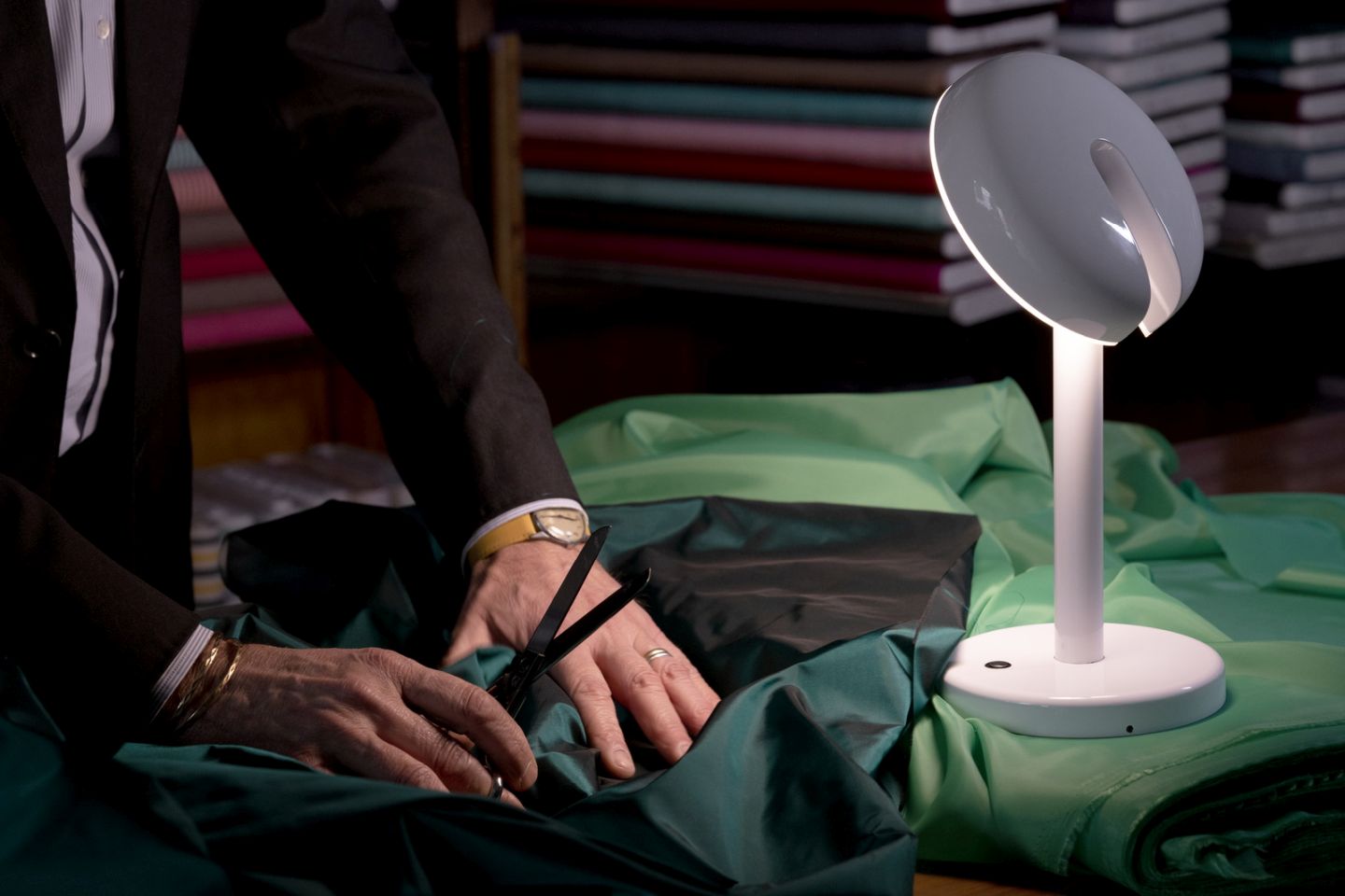 Cabriolette Tischleuchte von Martinelli Luce beleuchtet Schneider bei der Arbeit an Stoff.