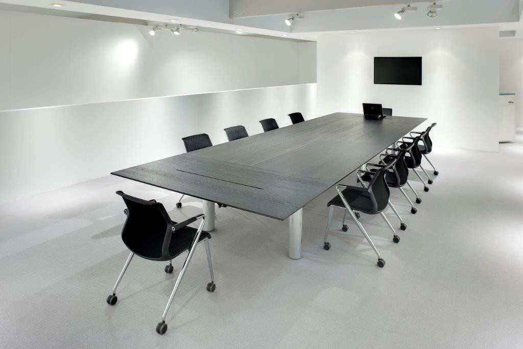 Konferenzraum mit großem, dunklen Holztisch und schwarzen Unix Chair Vierbeinstühlen auf Rollen von Vitra.