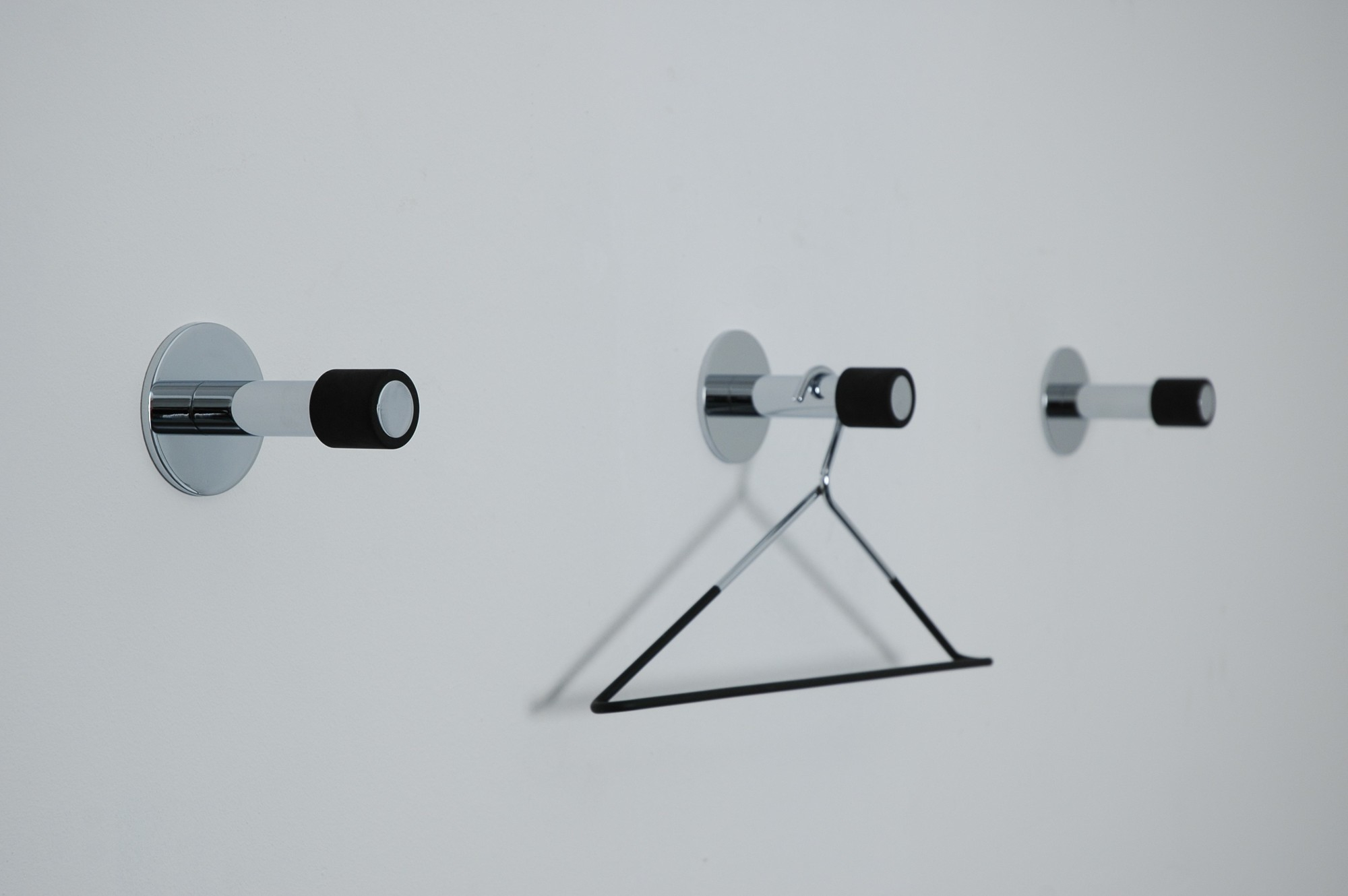 Drei Port Wandhaken an weißer Wand, einer mit Kleiderbügel. Moderner Wandhaken für Garderobe.
