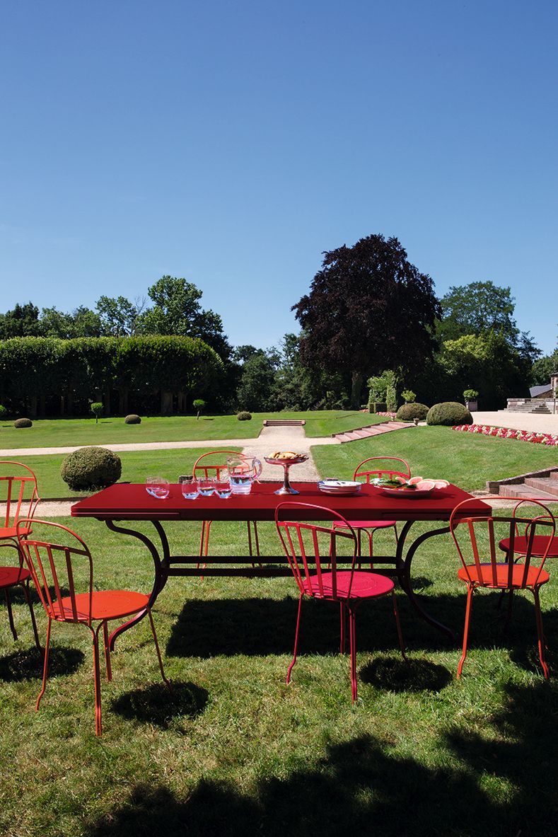 Roter Romane Tisch von Fermob im Garten, gedeckt mit Geschirr und Gläsern. Outdoor-Möbel.