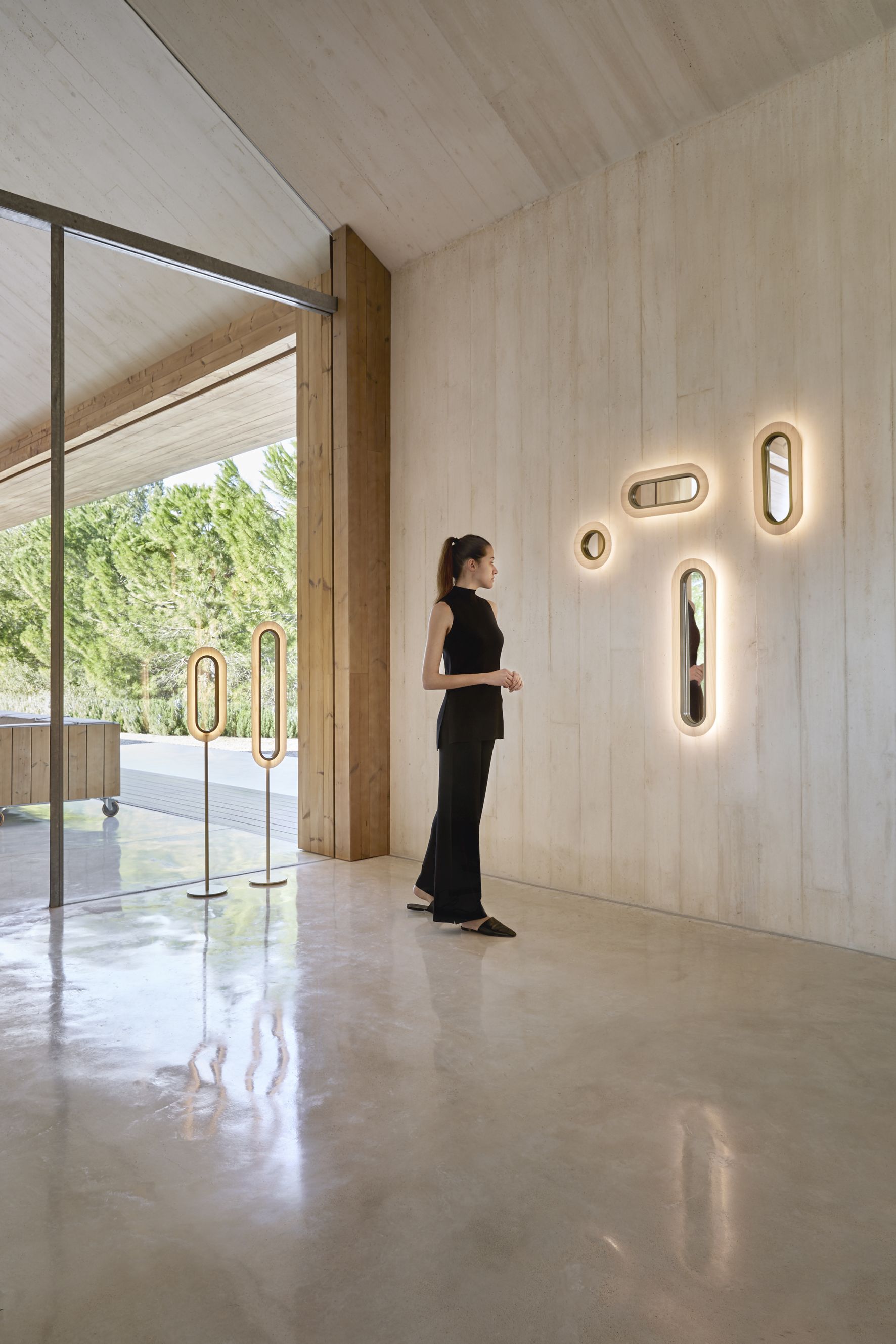 LZF Lamps Lens LED Wandleuchten: Ovale, hellrosa Lampen mit goldenem Metallring an Betonwand.