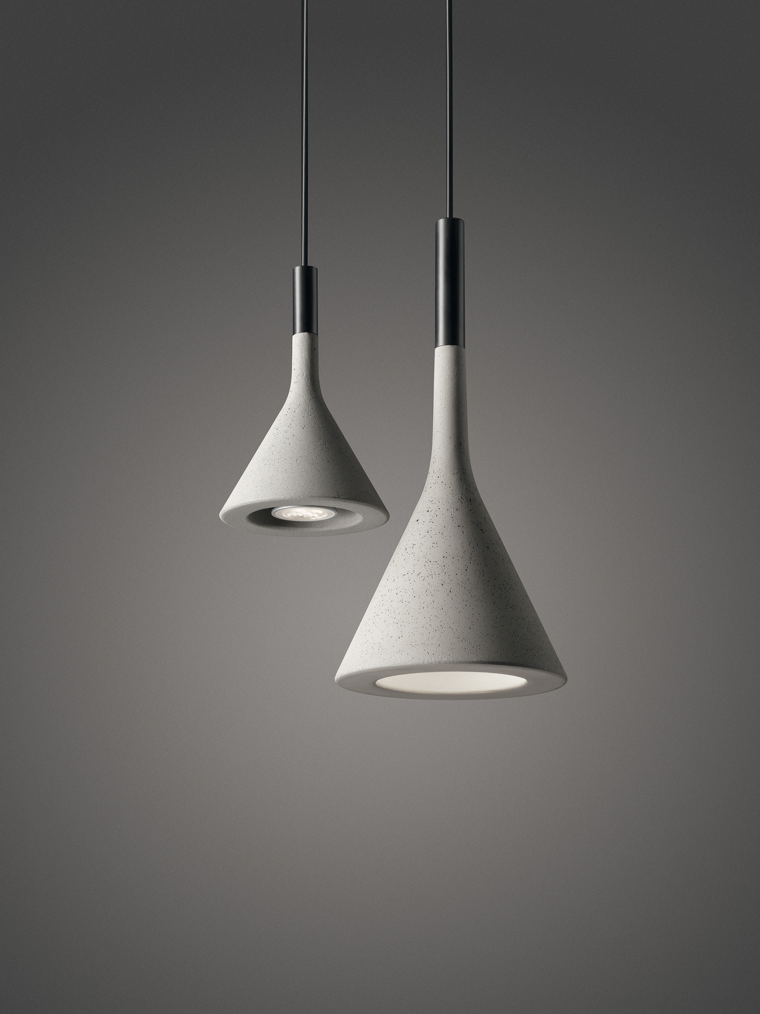 Zwei graue Aplomb Pendelleuchten von Foscarini mit Kegelform und Beton-Optik hängen von der Decke.